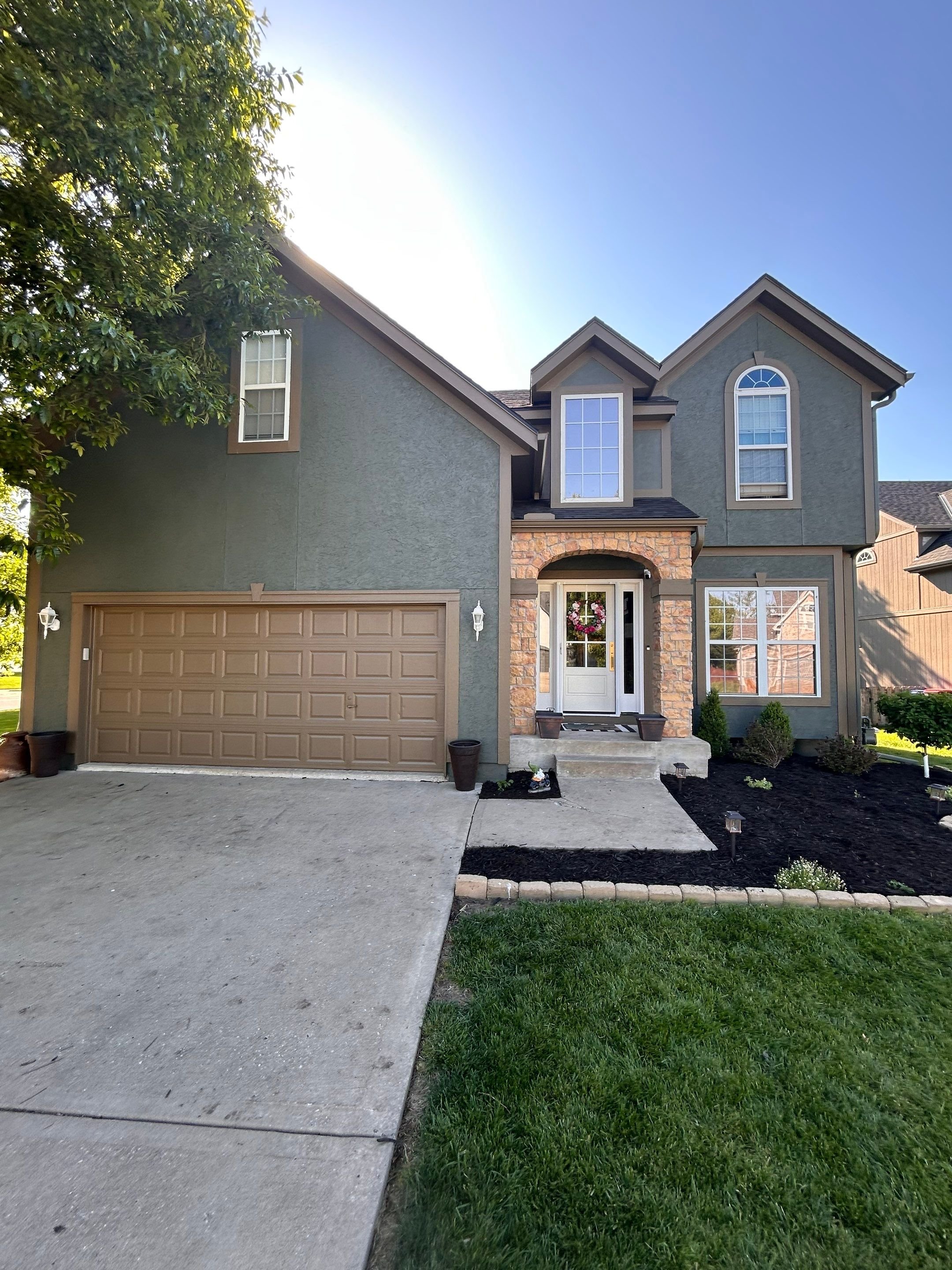 Two-story stucco home exterior painted in a rich sage green with warm tan trim by EverPro Painting — Kansas City residential painters