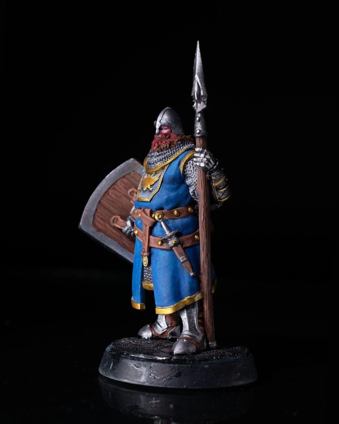 Miniature figurine of a medieval knight wearing blue and gold armor, holding a shield in one hand and a spear in the other, with a black background.