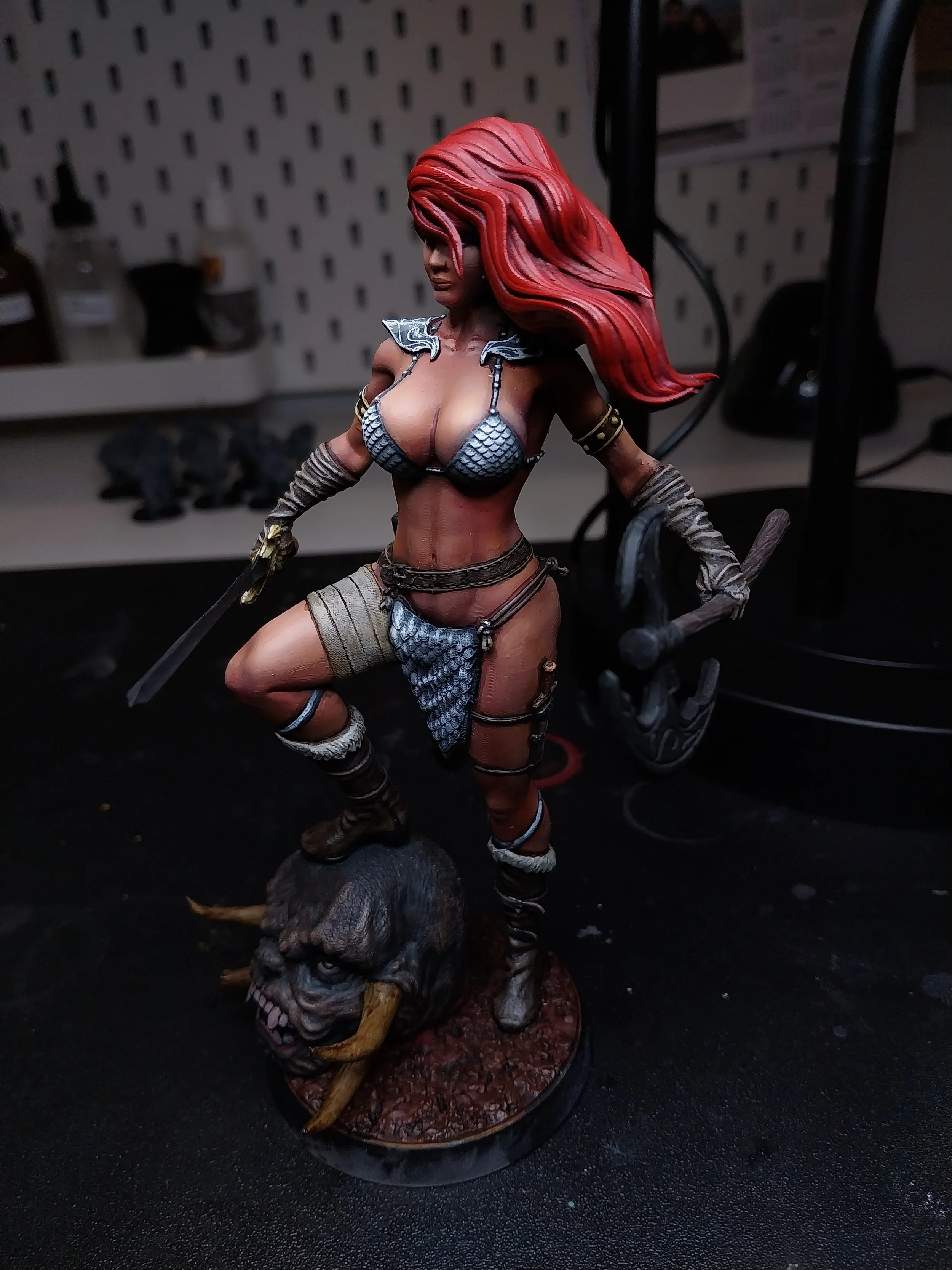A detailed figurine of a female warrior with long red hair, armor, and weapons, standing on a base with a beast's head.