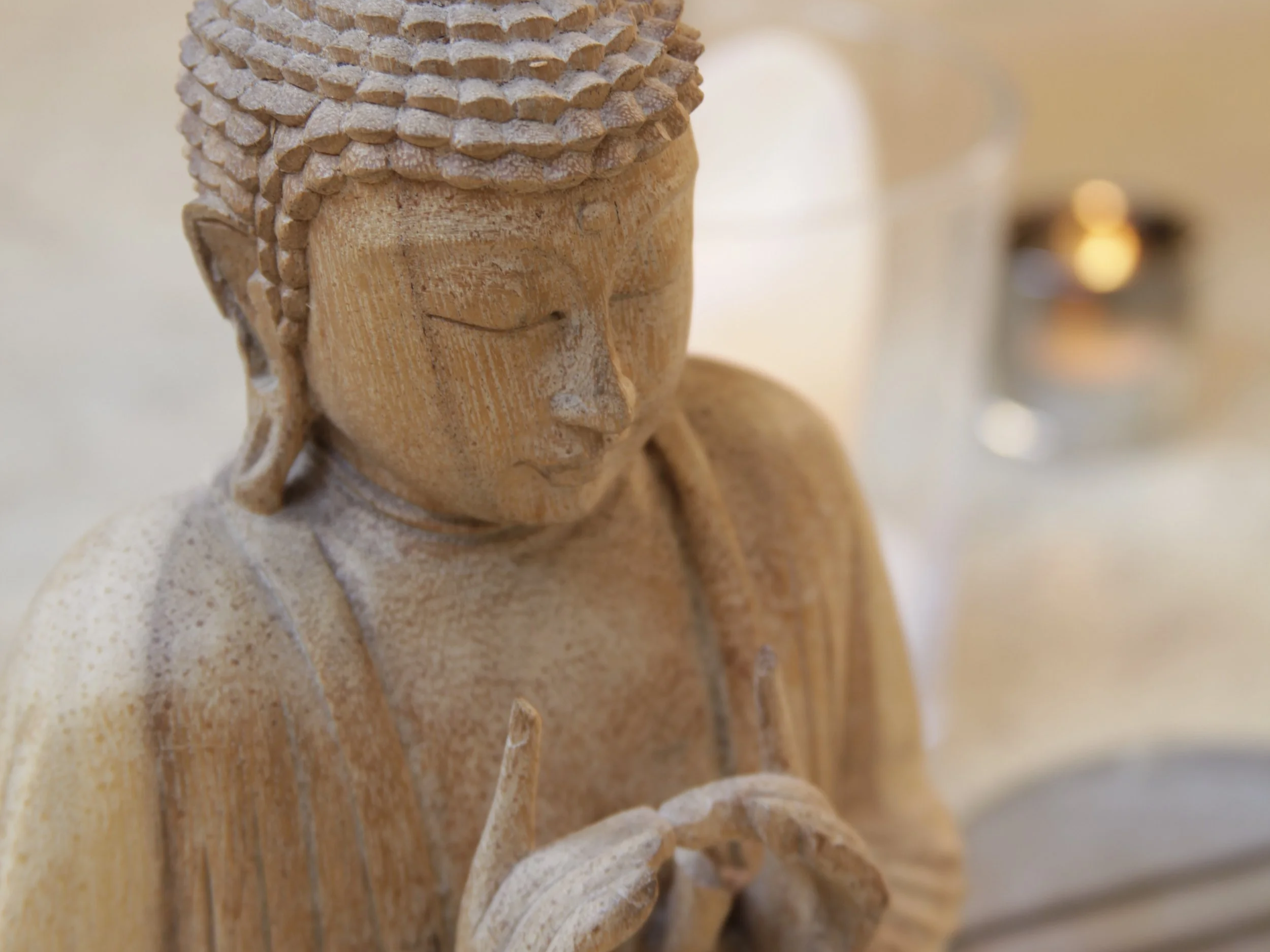 Eine geschnitzte Holzfigur eines Buddha mit geschlossenen Augen und einer friedlichen Haltung, die einen kleinen Gegenstand in den Händen hält.