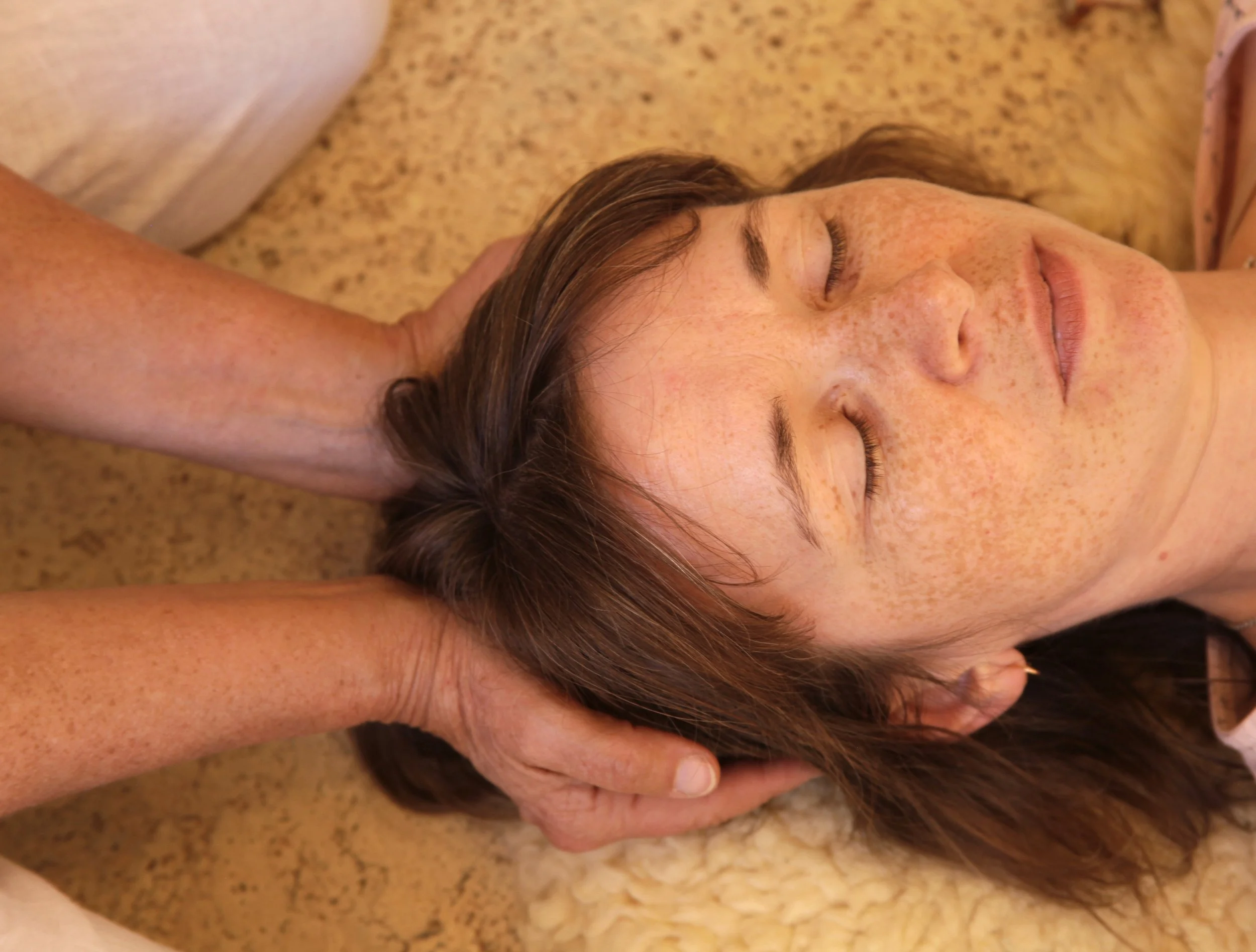 Frau liegt auf dem Rücken, erhält eine Kopfmassage.