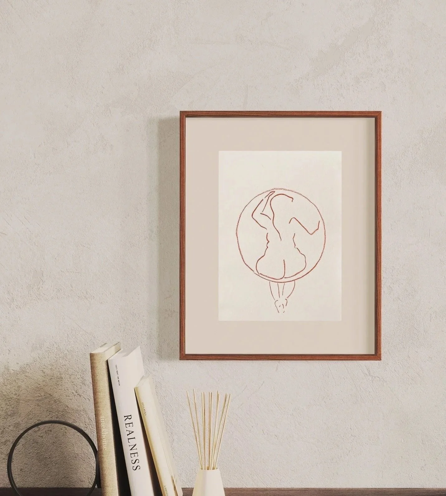 Minimalist line drawing of a woman in a circle, framed and hung on a wall, with books and a reed diffuser on a shelf below.