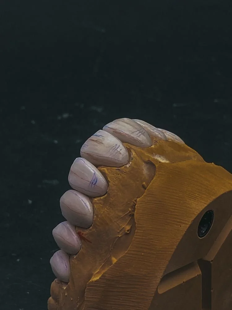 Close-up of a brown sculpture of a hand gripping a piece of wood or similar material, set against a dark background.