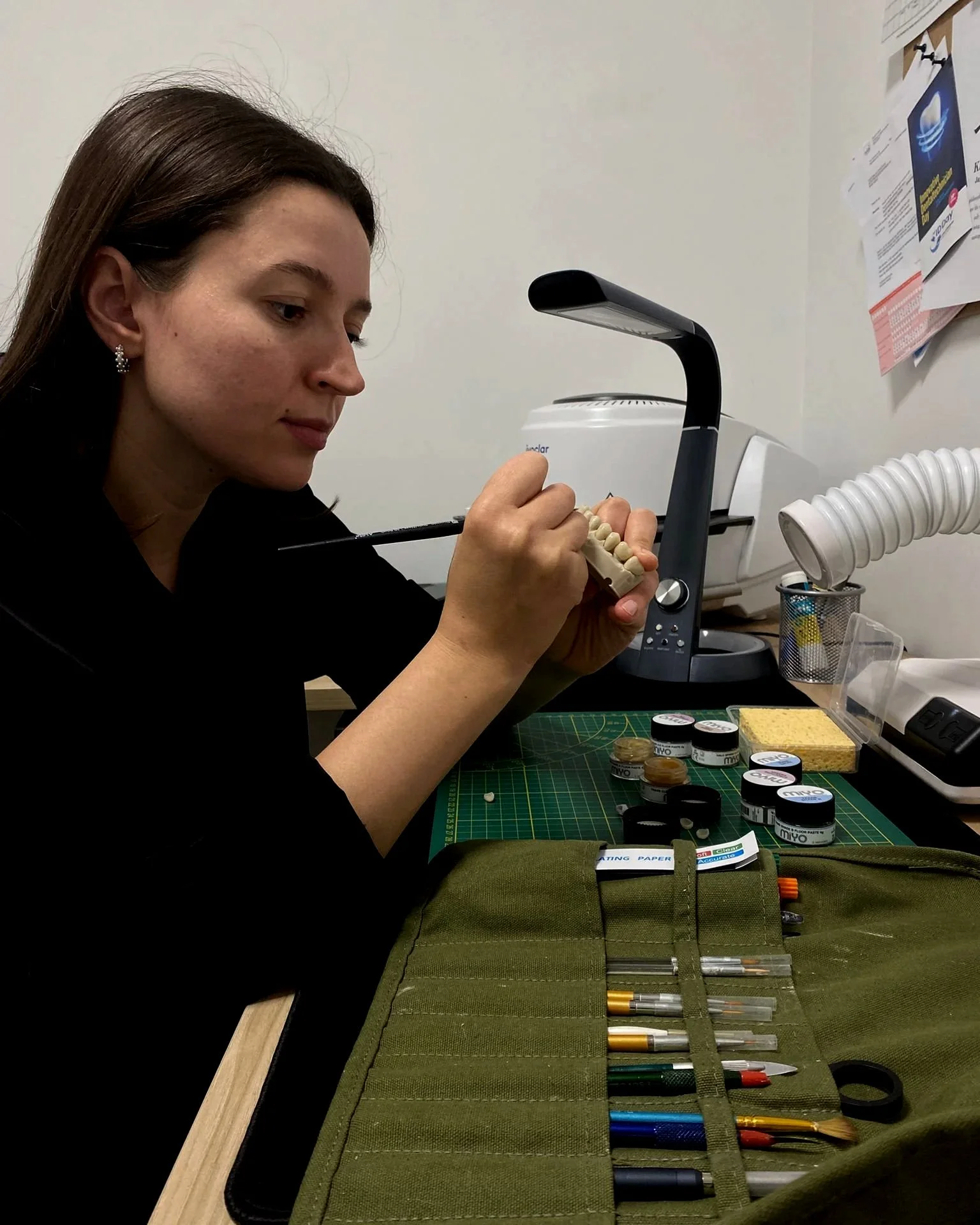 Een vrouw werkt aan een set tanden, met verschillende gereedschappen en tandpasta op de tafel.