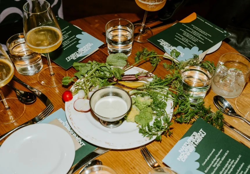 Table setting with wine glasses, water glasses, plates, cutlery, and a centerpiece of greens and radish. Menus are on the table.