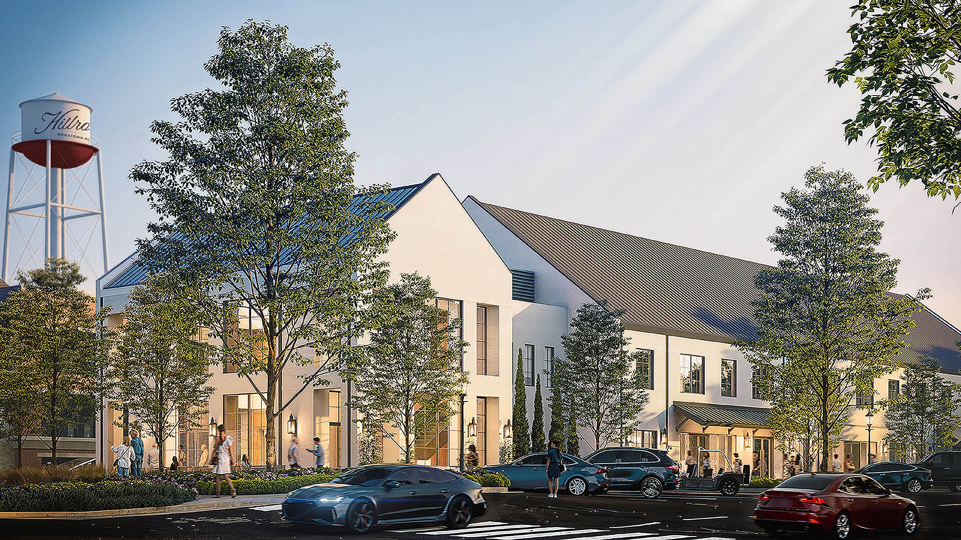 A modern white building with large windows and a sloped roof, surrounded by trees and people walking on the sidewalk, with cars parked and driving along the street in front.