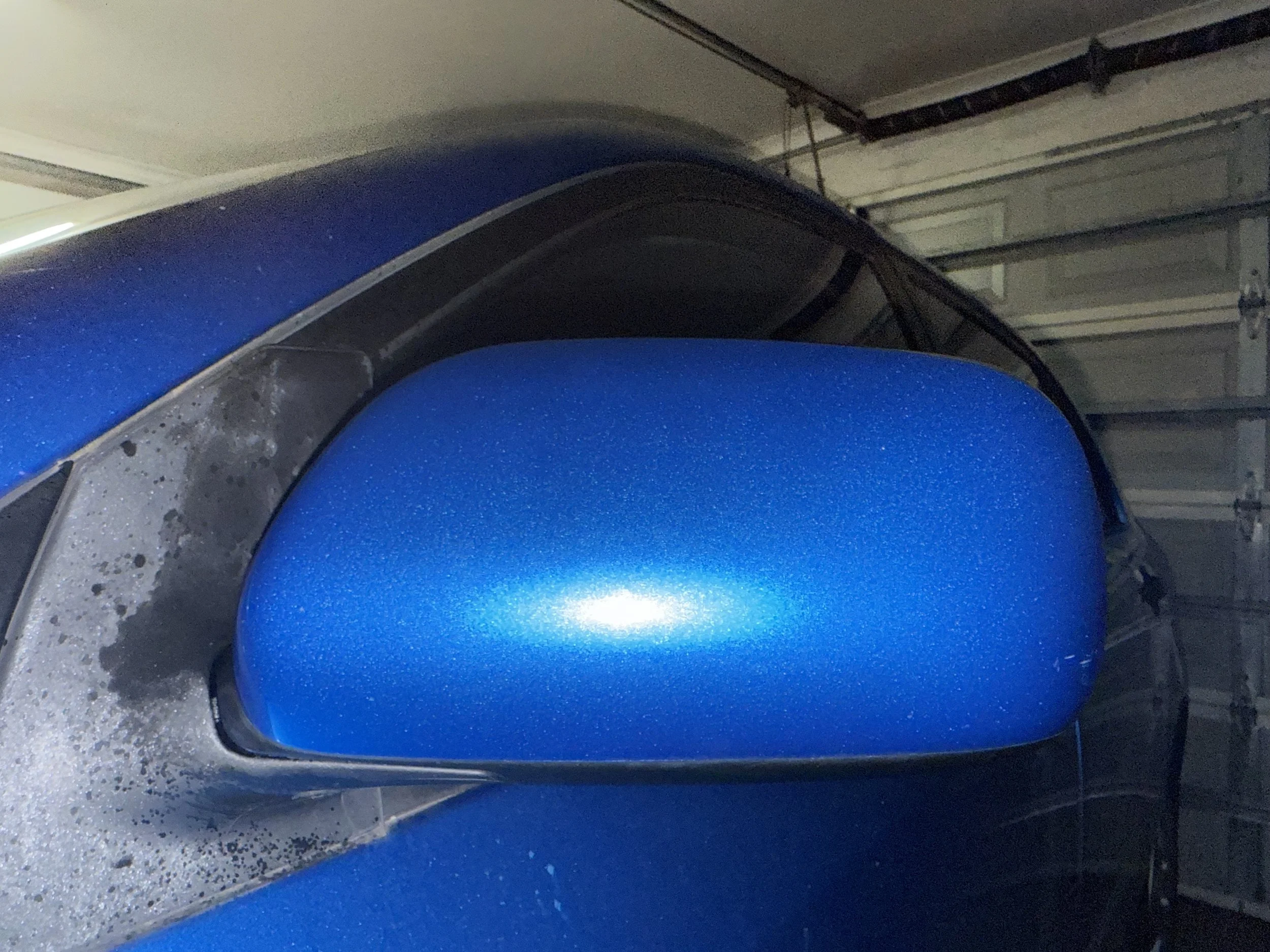 Close-up of a blue car's side mirror with a reflective, shiny surface in a garage.