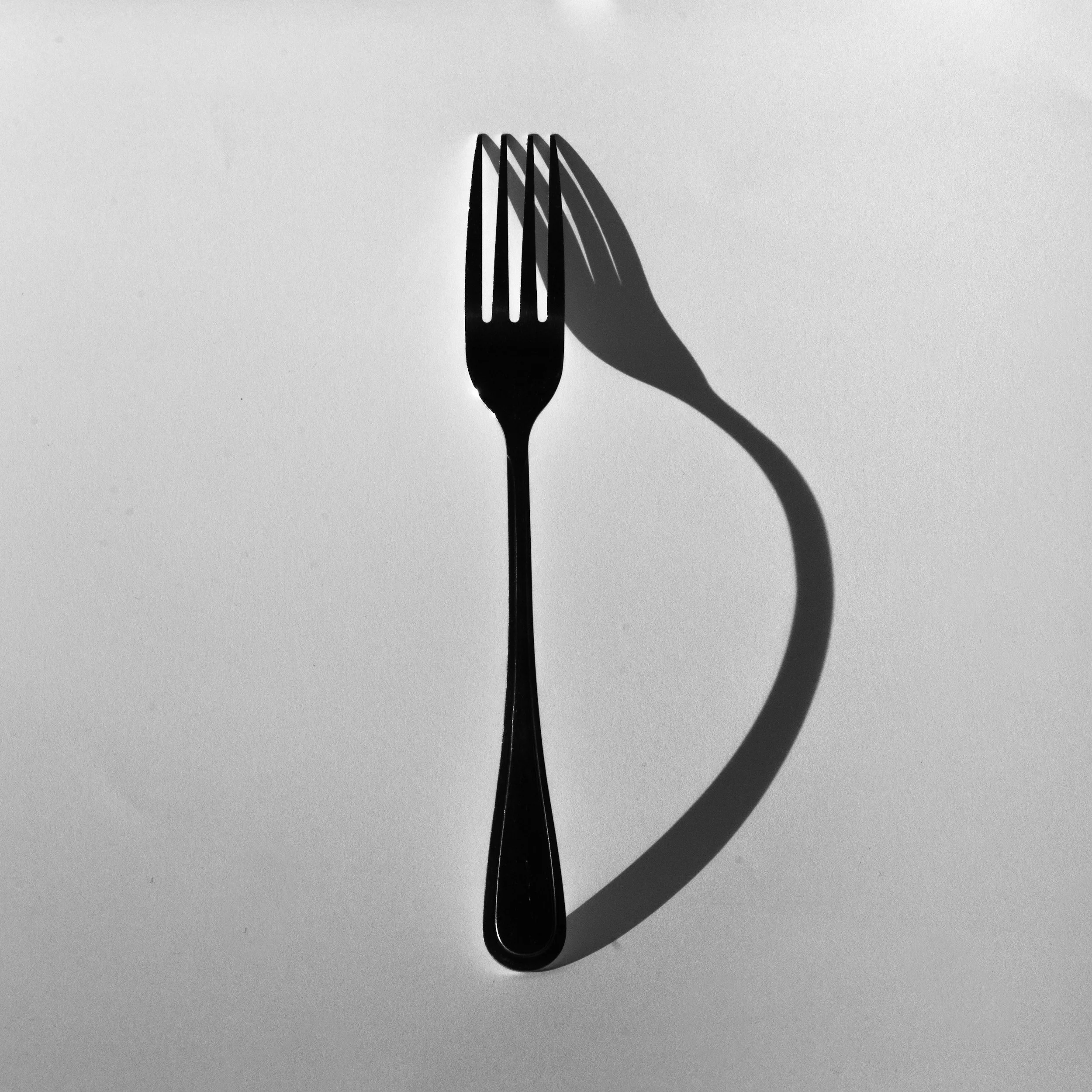 Shot of a bent fork from above casting a shadow on a plain light background.