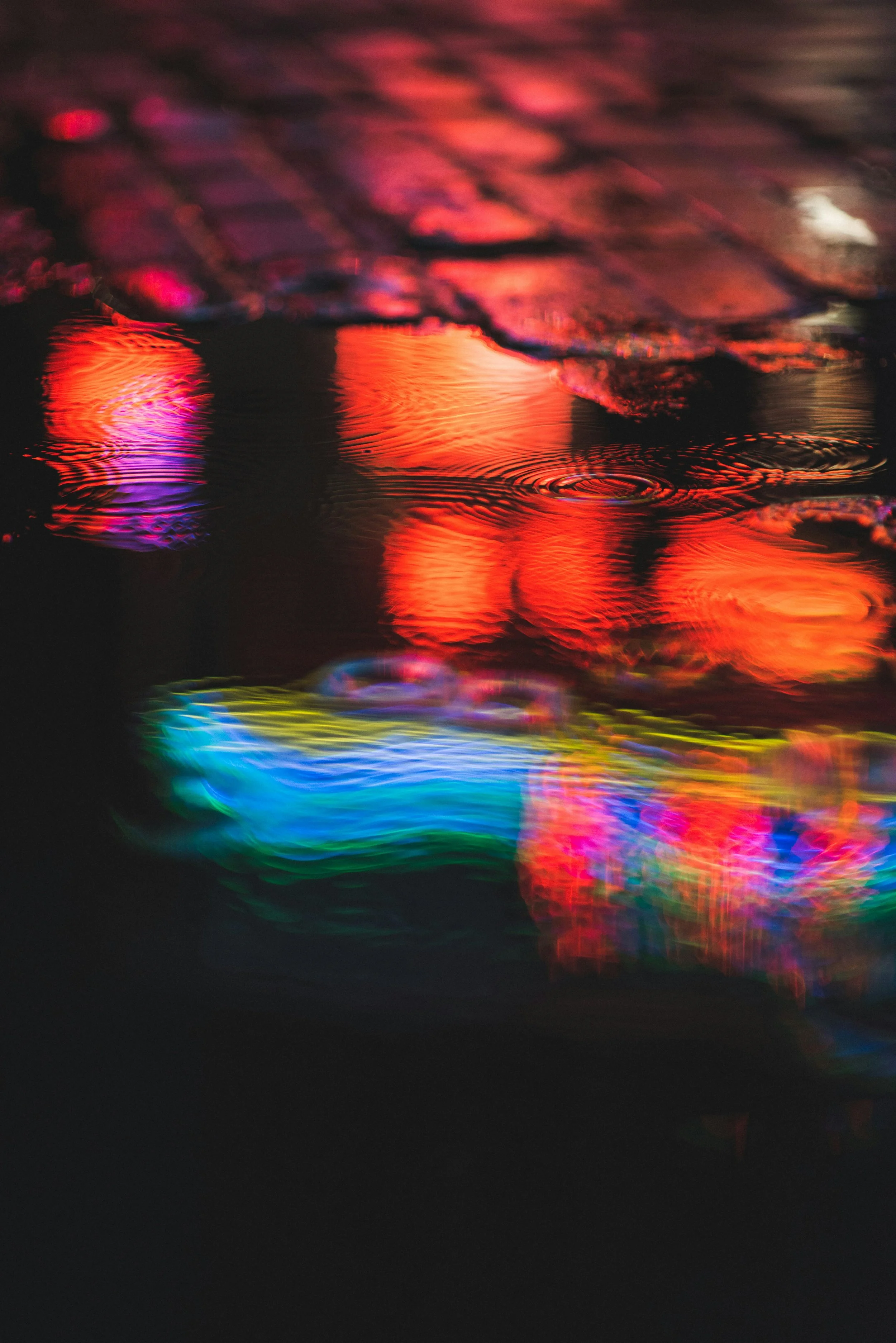 Colorful reflections of neon lights on wet pavement at nighttime.