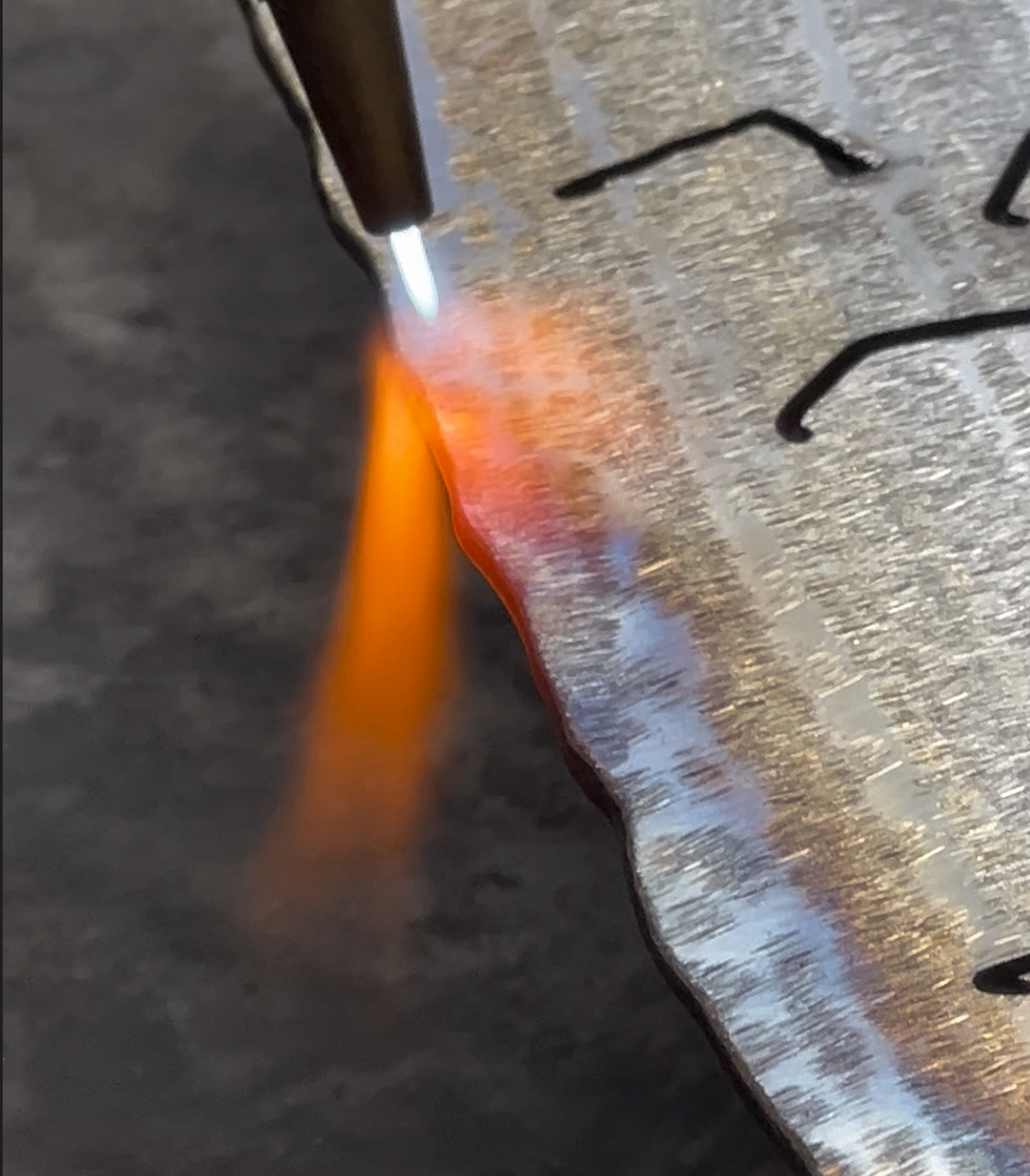 Close-up of a metal object being welded or soldered, with a bright orange and yellow flame or spark emitting from the welding tool.