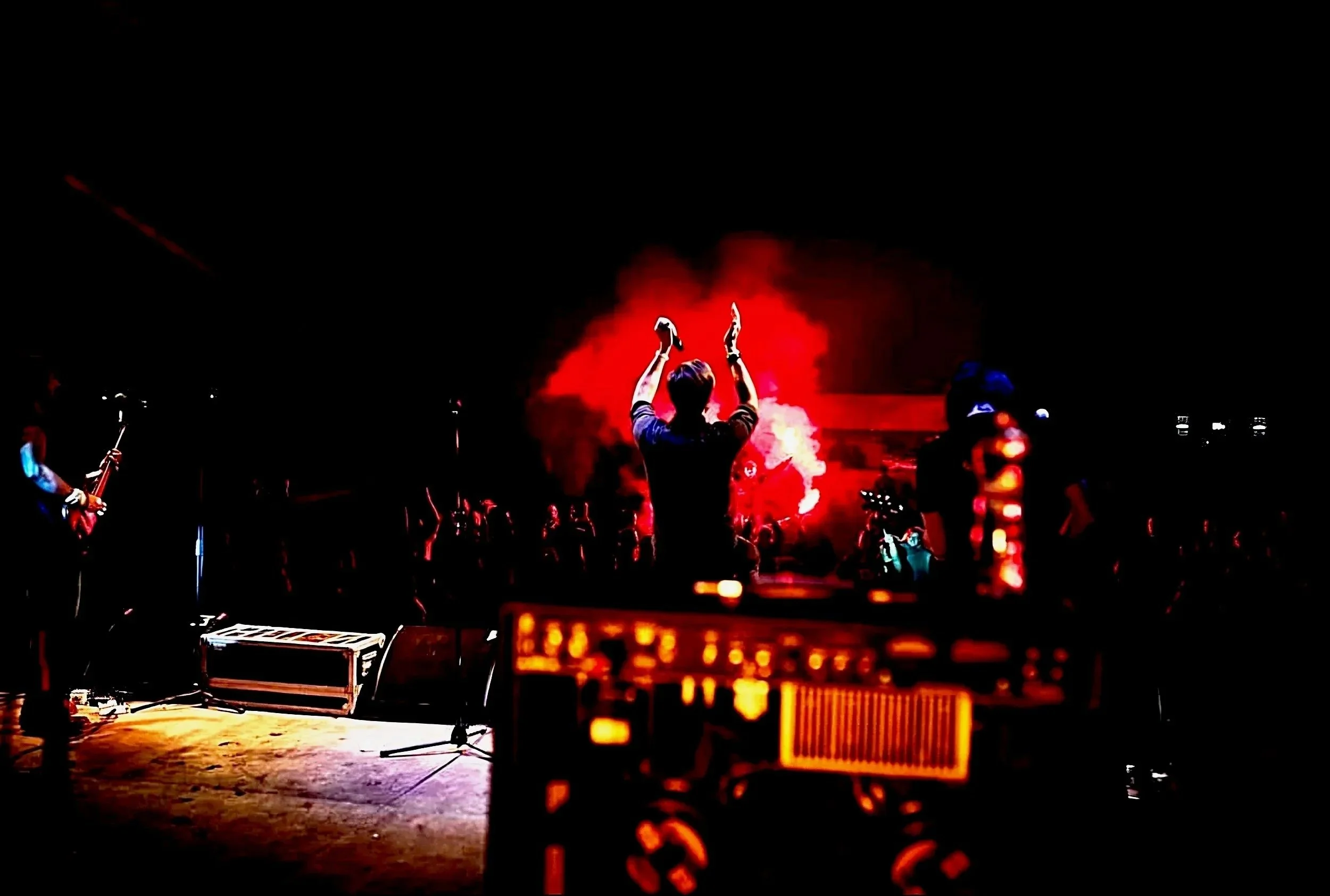 Band on stage at a small venue facing the audience., the lead singer has his hands in the air clapping