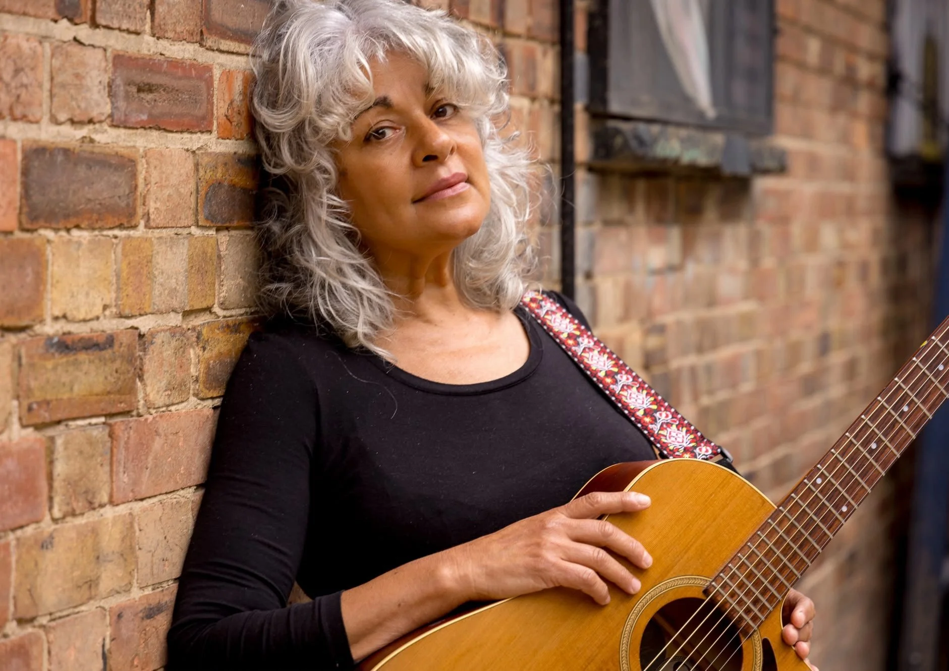Woman with beautiful touseld white hair, leaning on wall with her guitar.