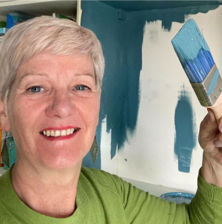 Photo of Josephone holding a paintbrush in front of a half-painted wall