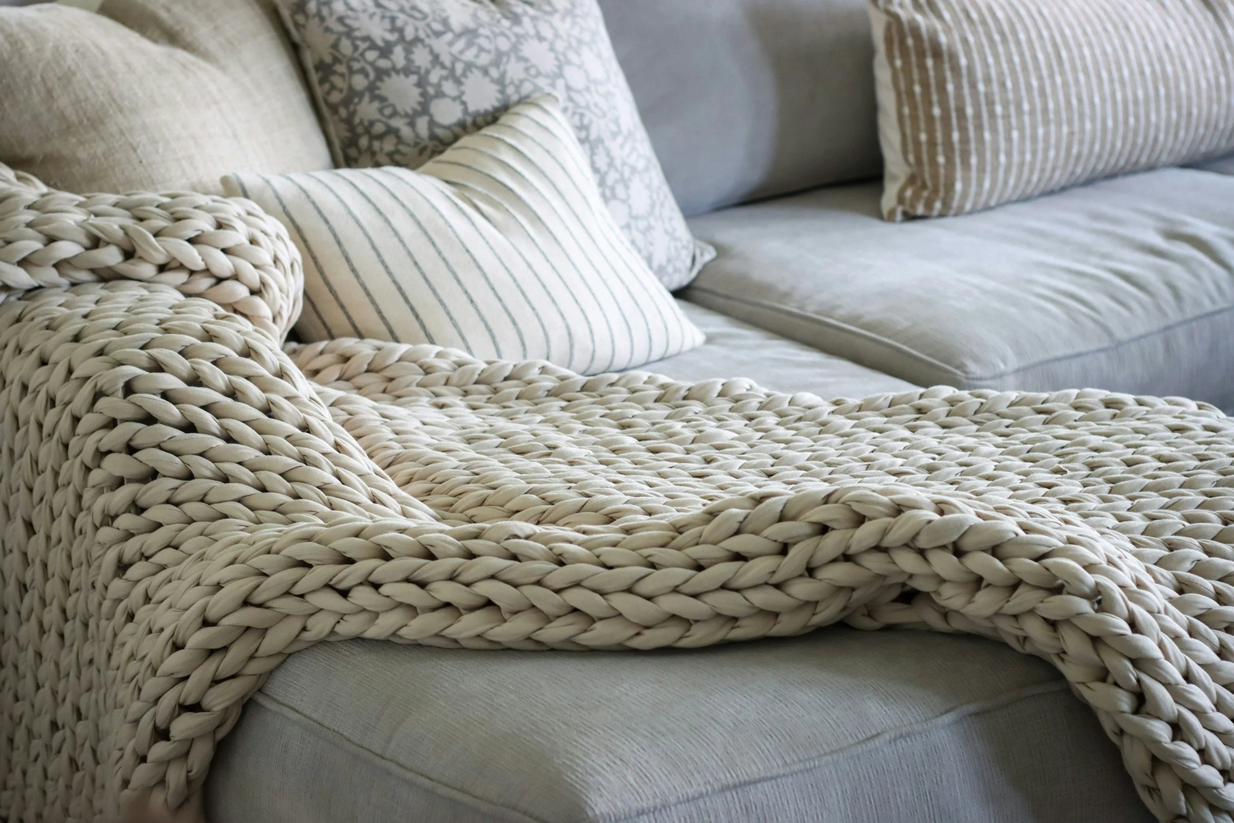 A light-colored sofa with plush cushions and a chunky knit throw blanket.