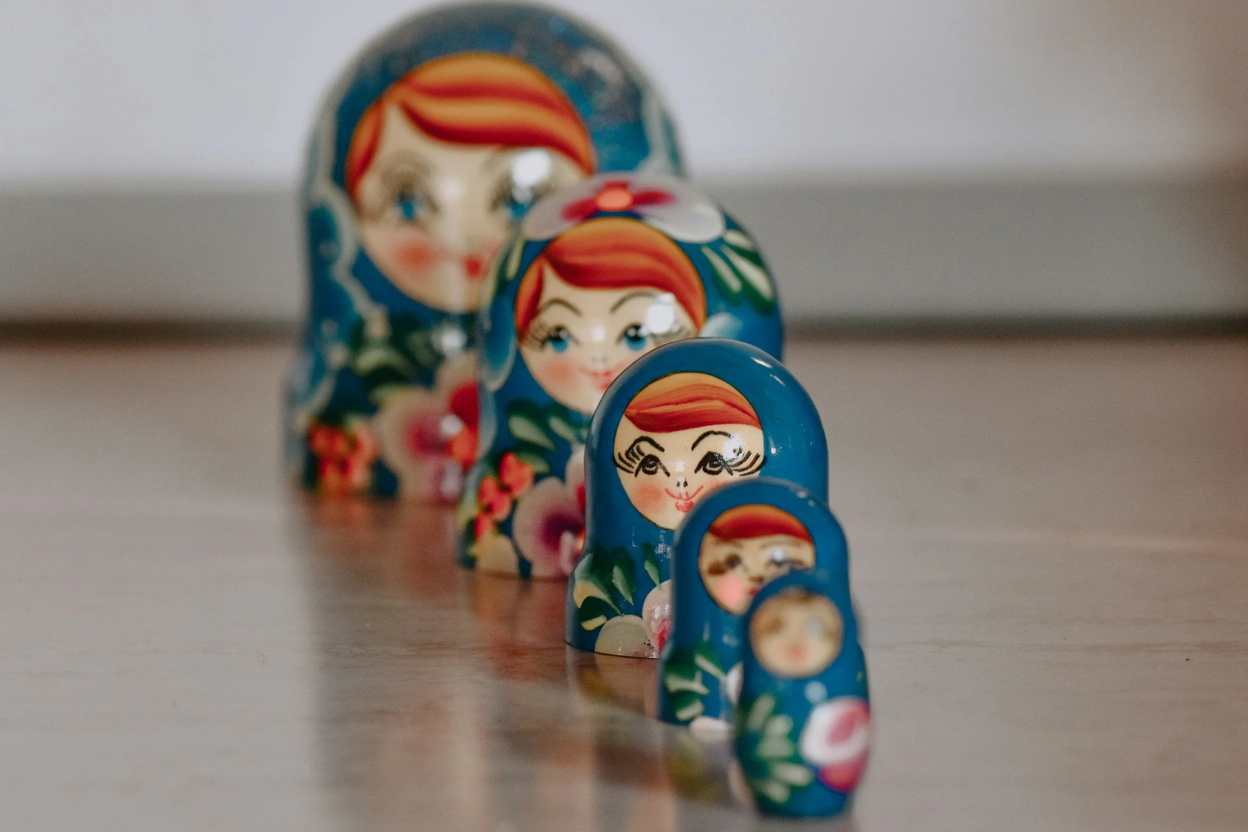 A line of five Russian nesting dolls, known as matryoshka dolls, arranged from largest in the back to smallest in front, with traditional floral and facial designs.