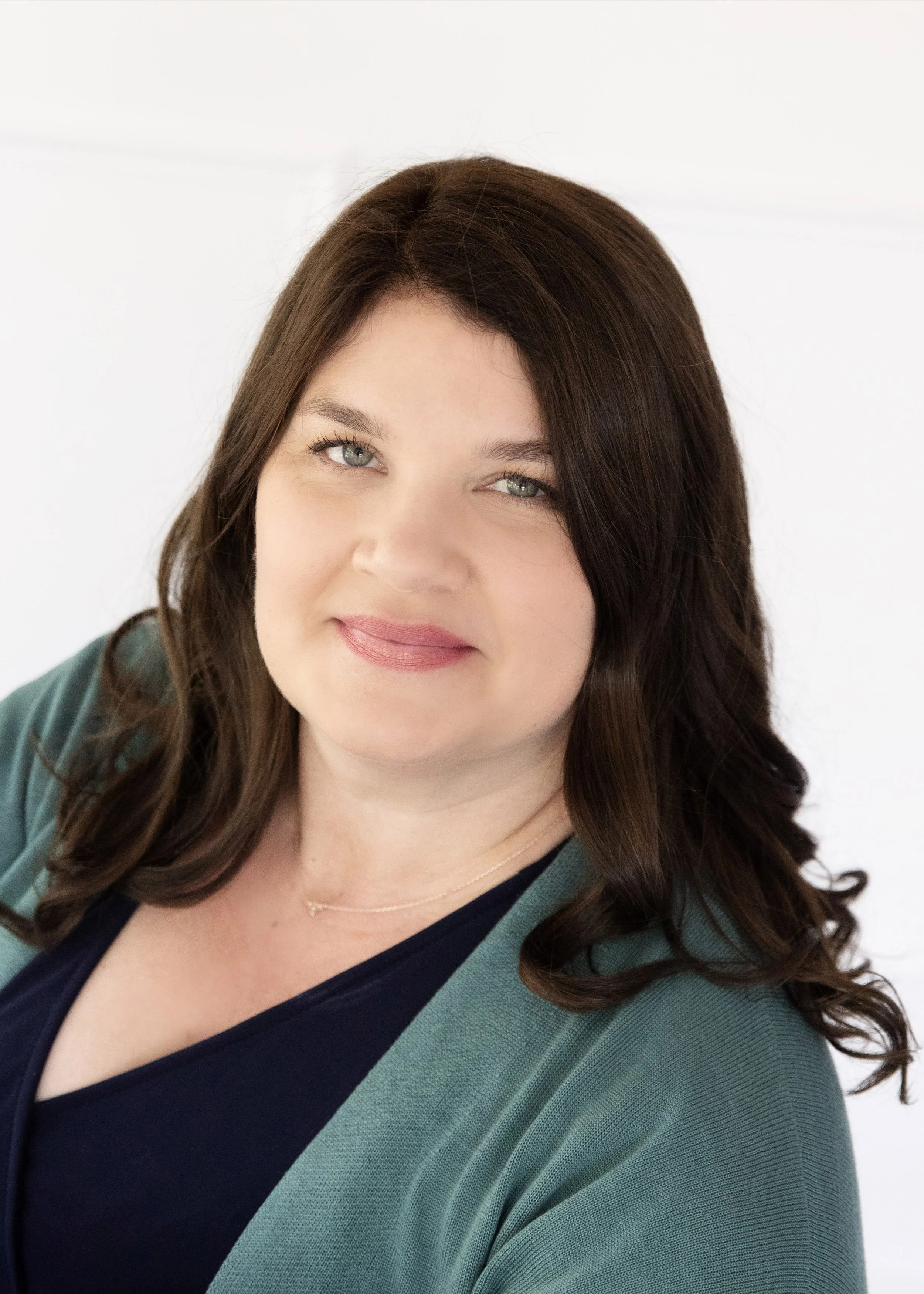 Portrait of a woman with shoulder-length brown hair, wearing a dark blue top and green jacket, against a white background.