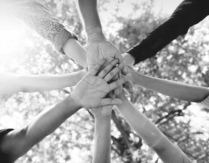 Multiple hands from diverse people stacking together in a circle outdoors.