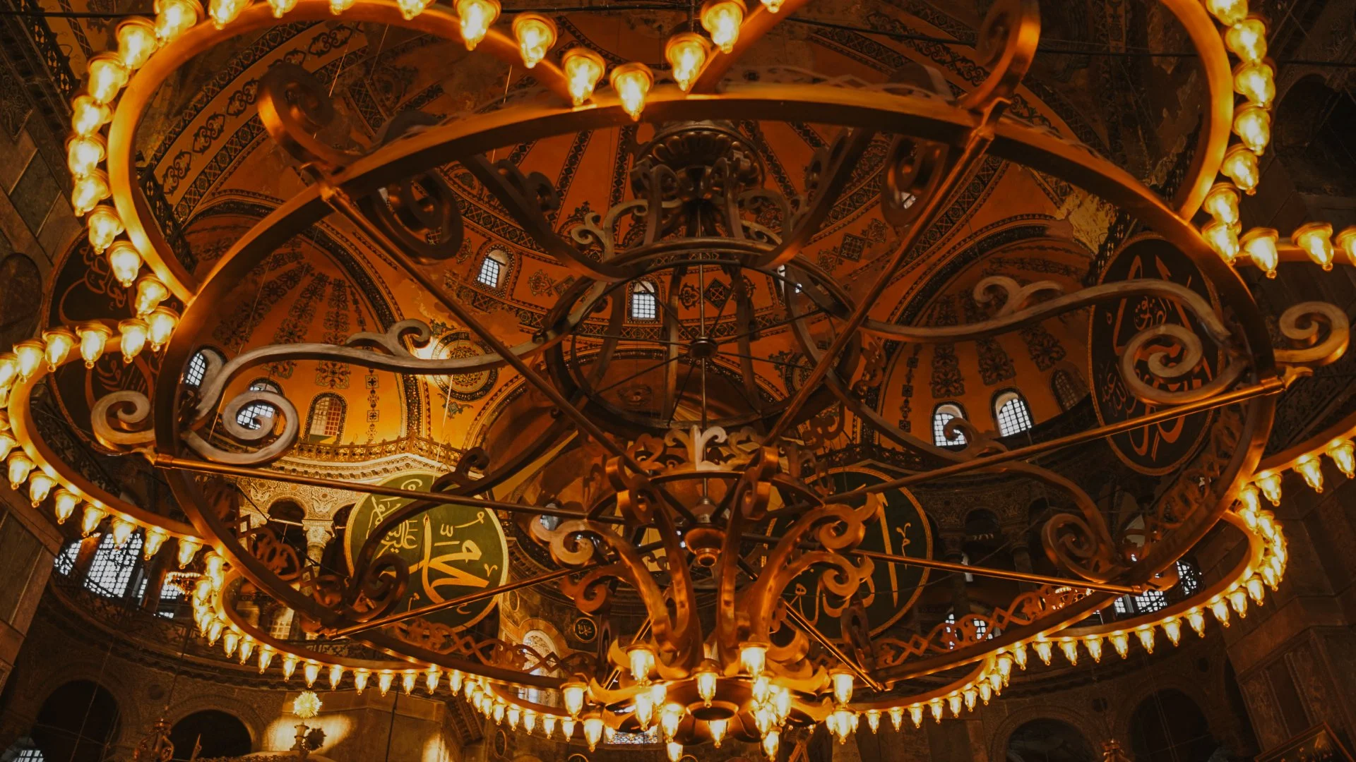 Ein prächtiger Kronleuchter mit vielen kleinen Lichter in einer Moschee, mit einem goldenen und schwarzen Dekor im Hintergrund.