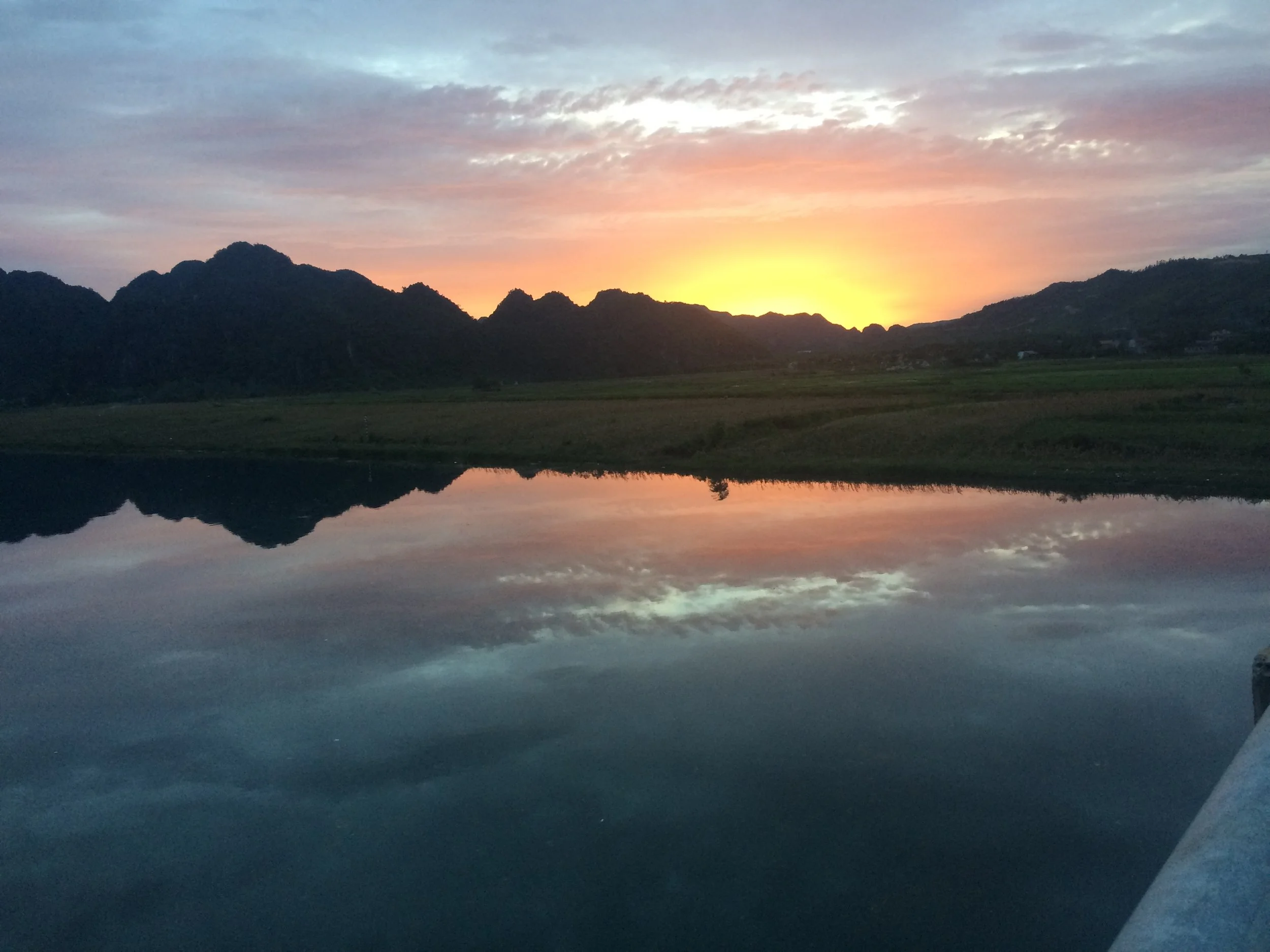 Phong Nha - Sunset over mountains reflected in a calm body of water with a partly cloudy sky. Deeply Peaceful. Relaxing. Healing.