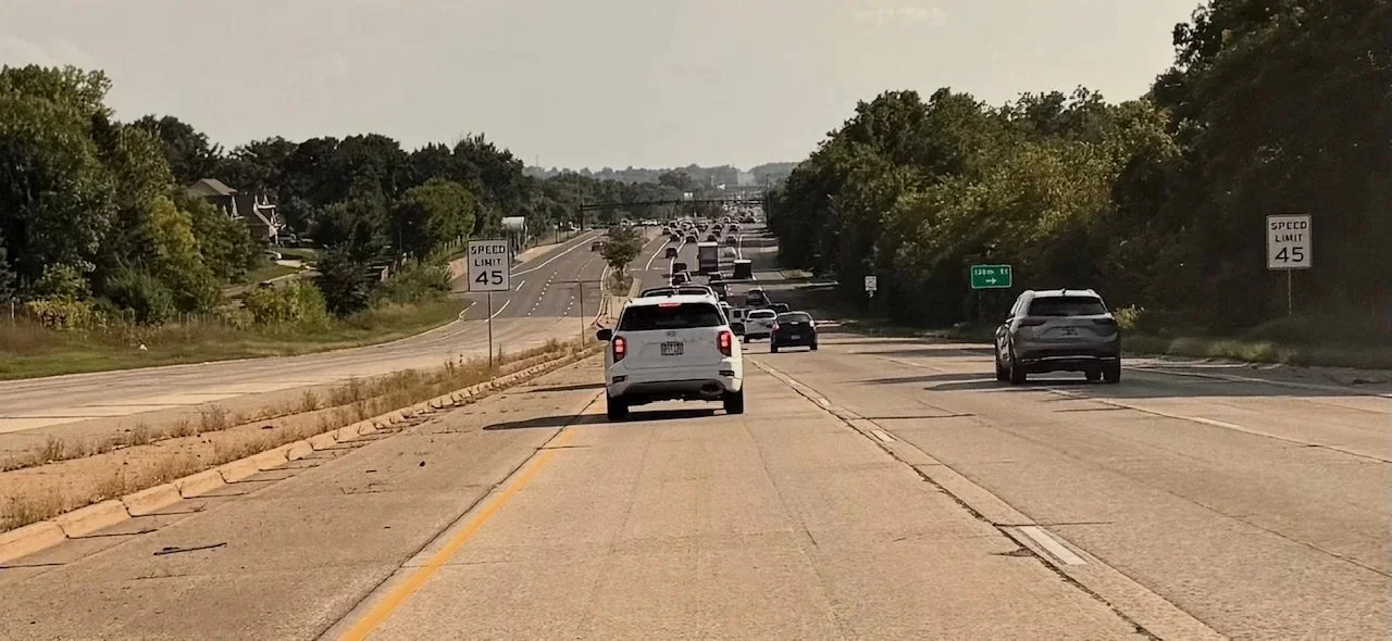 Southbound view of the City of Apple Valley, Minnesota, busy highway with multiple cars traveling in both directions, surrounded by green trees and a few signs indicating a speed limit of 45 miles per hour.