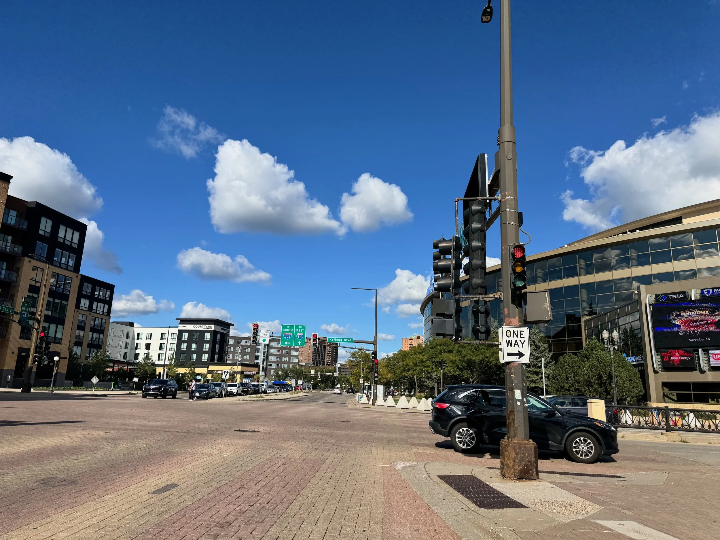 City of St. Paul, Xcel Energy Center, Grand Casino Arena, intersection with traffic lights, cars, and modern buildings under a partly cloudy blue sky.
