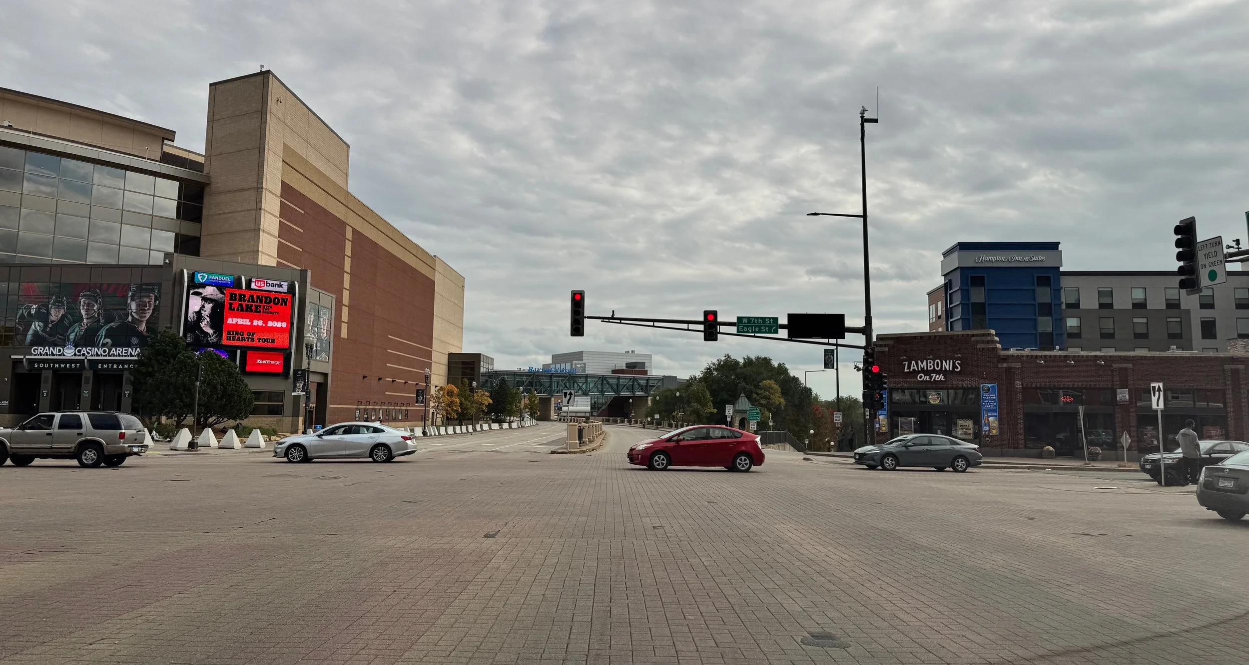 An urban street scene with traffic lights, several cars, and buildings, including a casino and a restaurant, overcast sky.