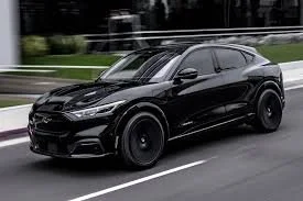 Black SUV driving on a road with trees and a fence in the background.