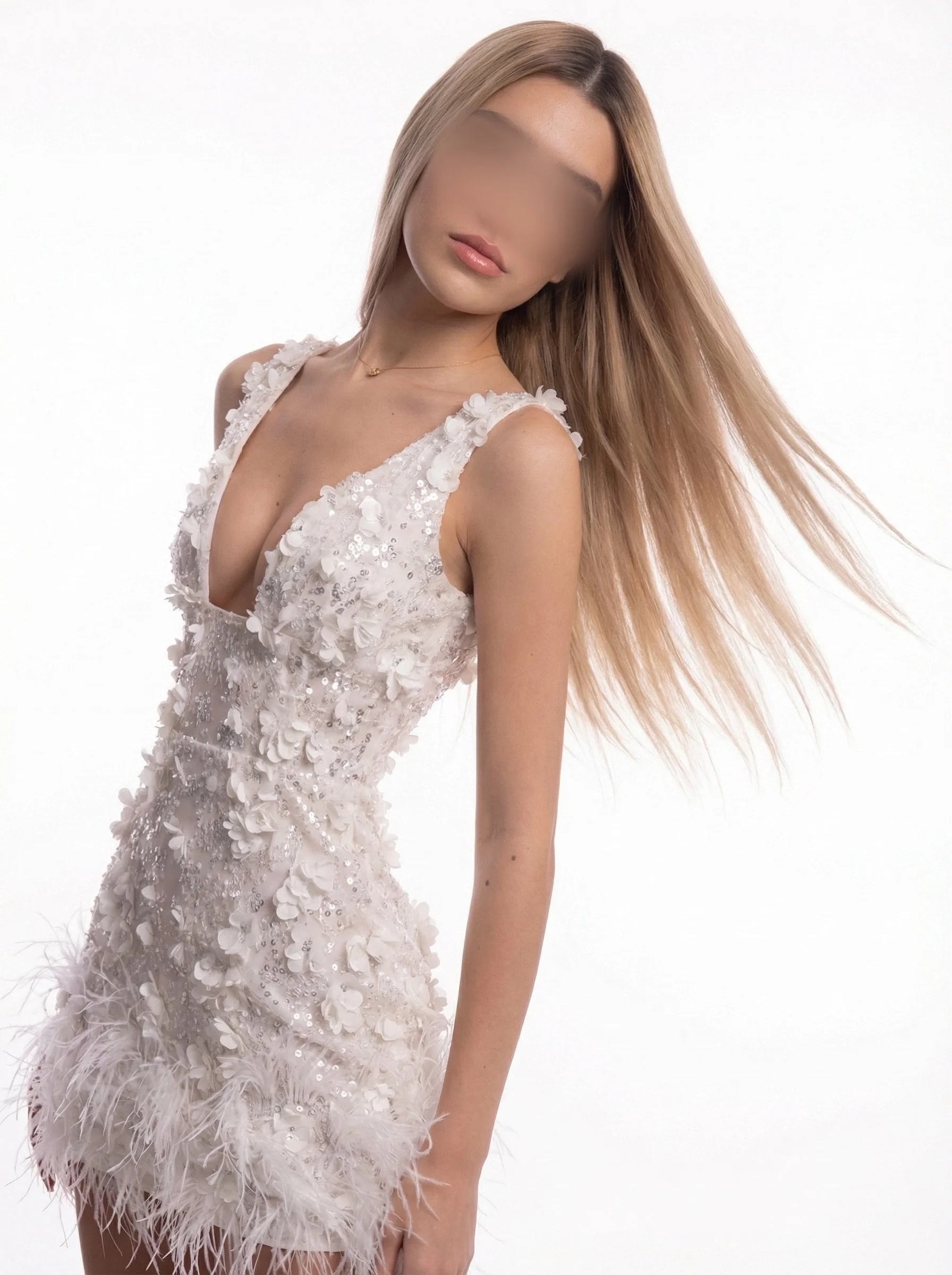 A woman wearing a white dress with floral embellishments and feather details, standing against a plain white background, with her long blonde hair flowing to the side.