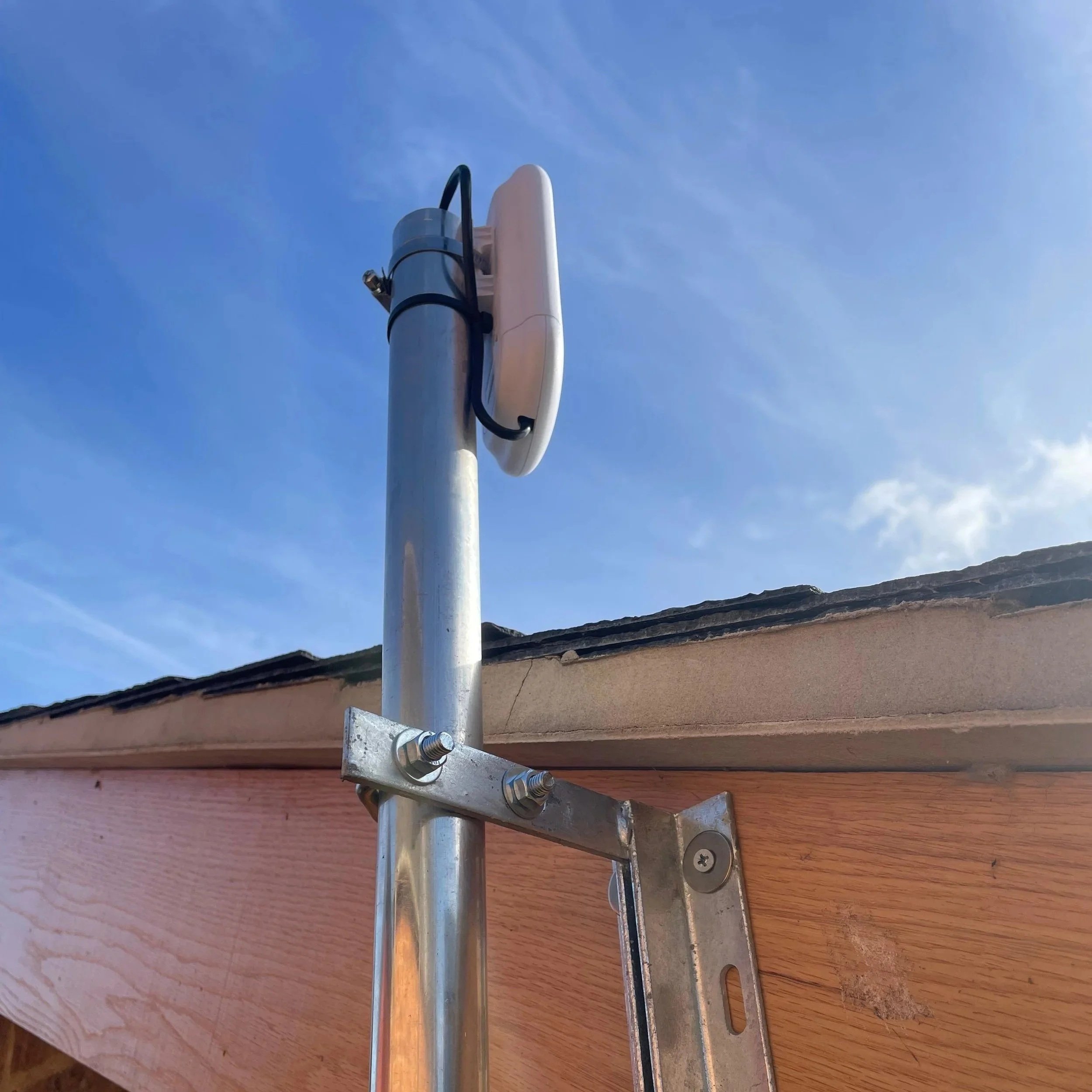 A close-up of an outdoor weather station or antenna mounted on a pole on the roof of a building with blue sky in the background.