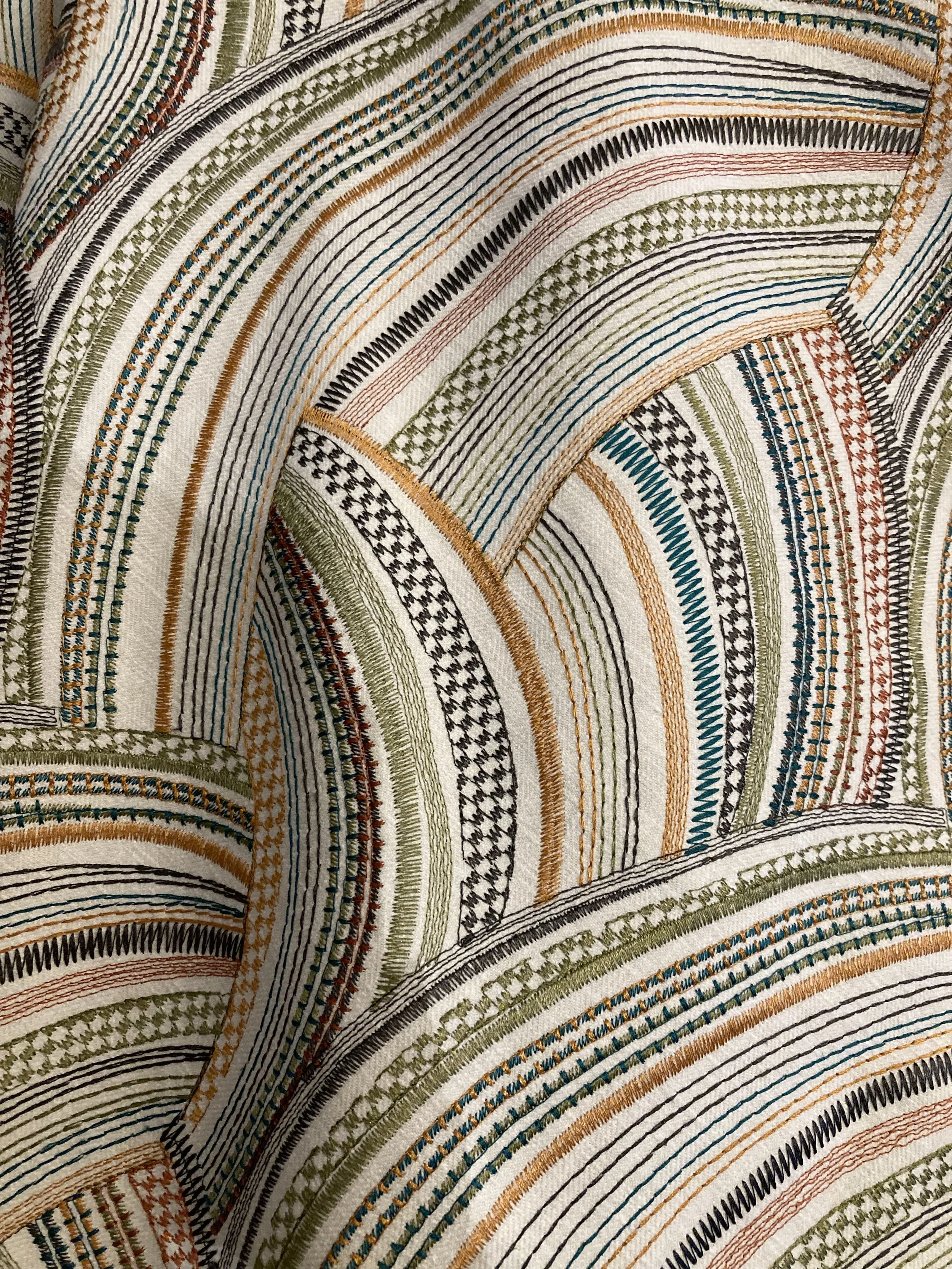Close-up view of a colorful embroidered textile with intricate patterns and curved lines in green, black, blue, orange, and red.