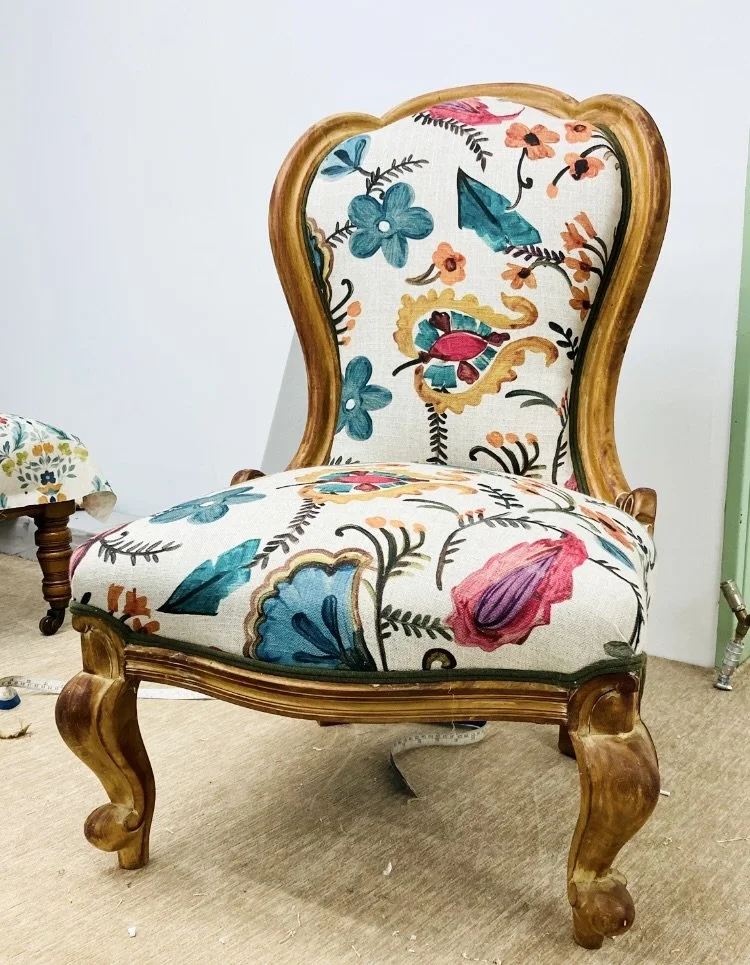 A vintage wooden chair with a floral-patterned upholstered back and seat, featuring blue, pink, orange, and green flowers.
