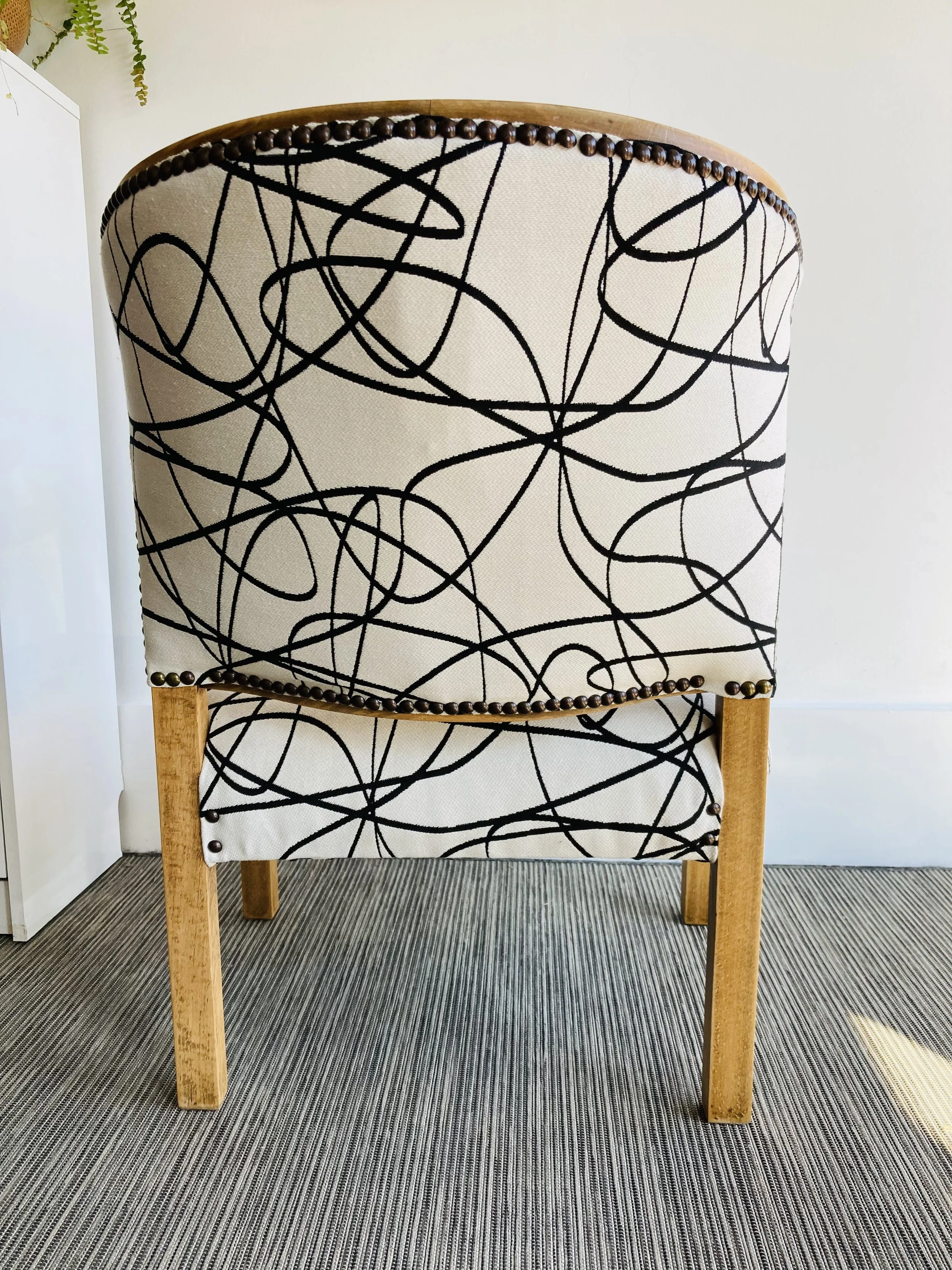 A high-back chair with a black and white abstract pattern, wooden legs, and decorative nailhead trim along the top edge and bottom of the backrest.