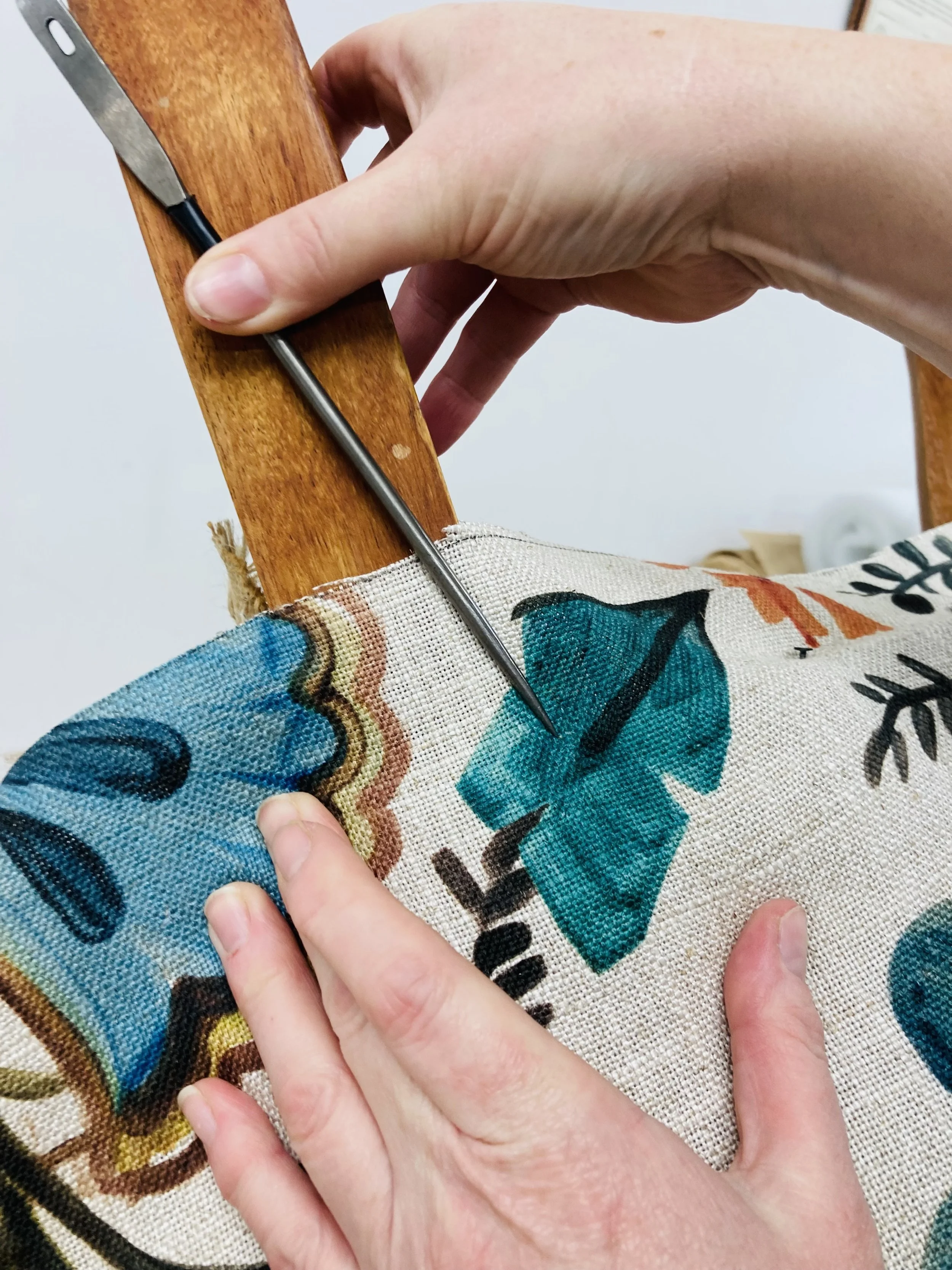 Person using a tool with a pointed tip to mark or cut fabric featuring colorful text and design, with a wooden surface behind.