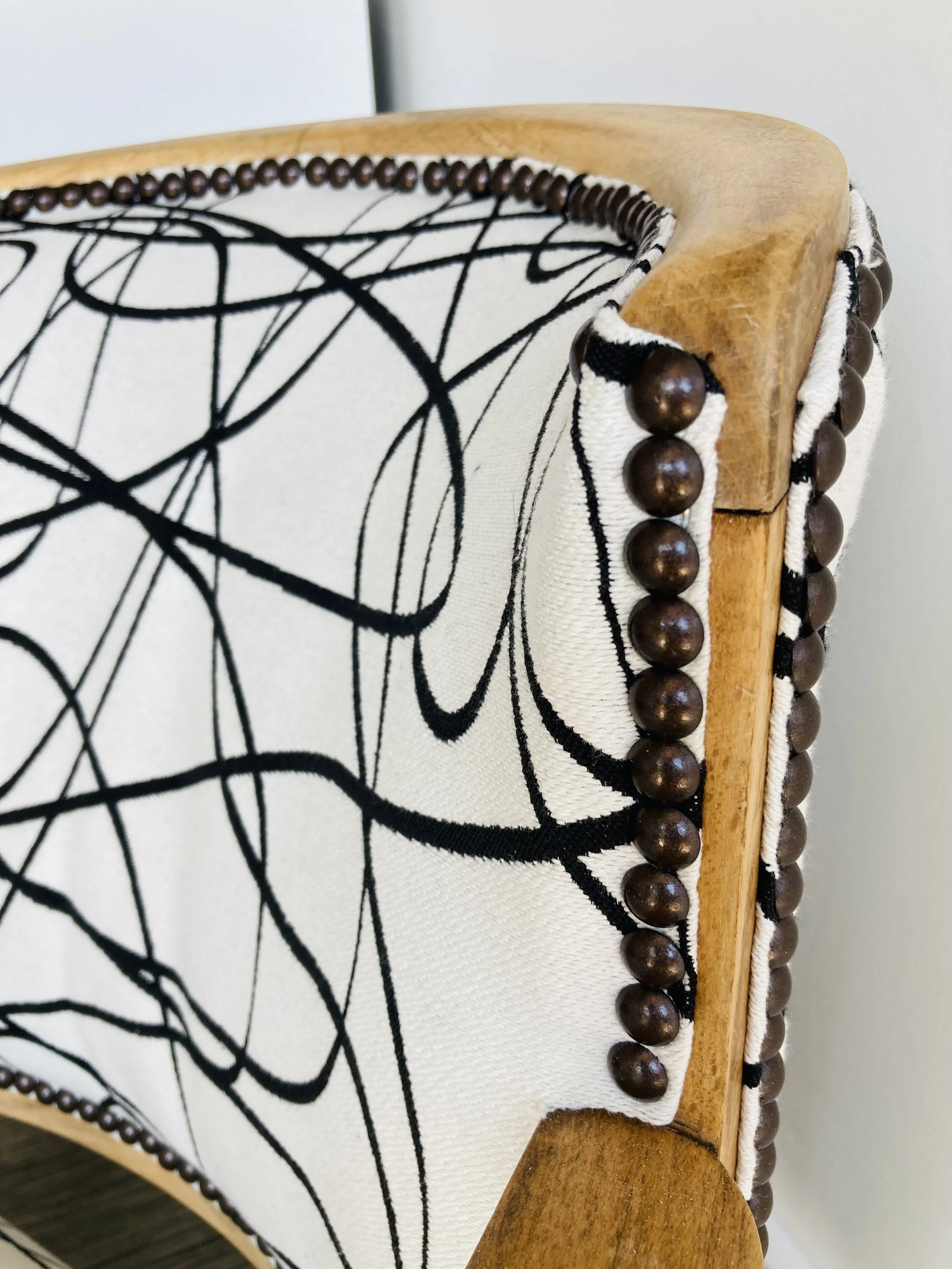Close-up of a modern chair with a wooden frame, fabric upholstery featuring black abstract line patterns, and decorative dark brown wooden beads along the edges.