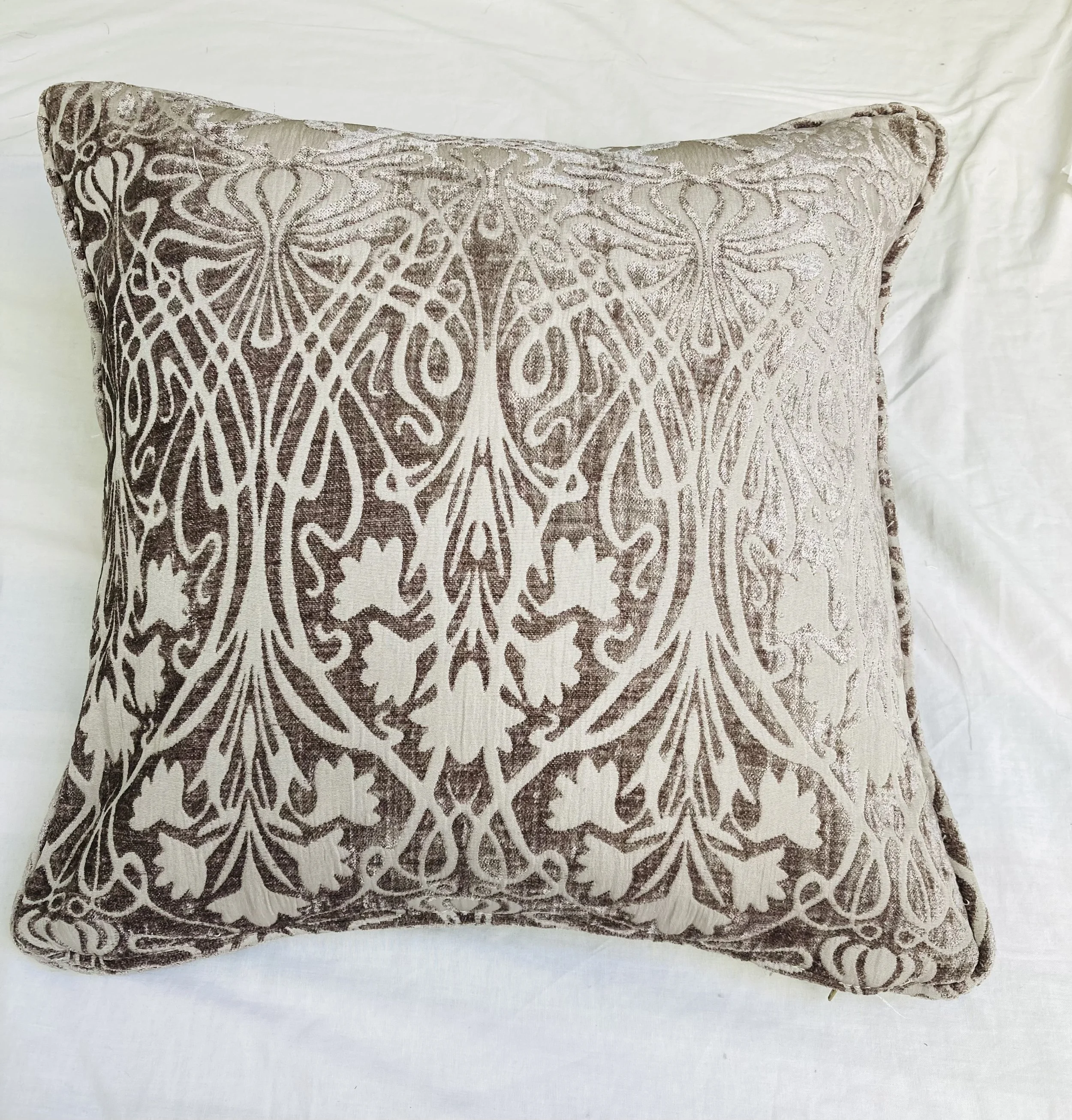 Decorative pillow with an intricate metallic silver embroidered pattern on a light background, placed on a white fabric surface.
