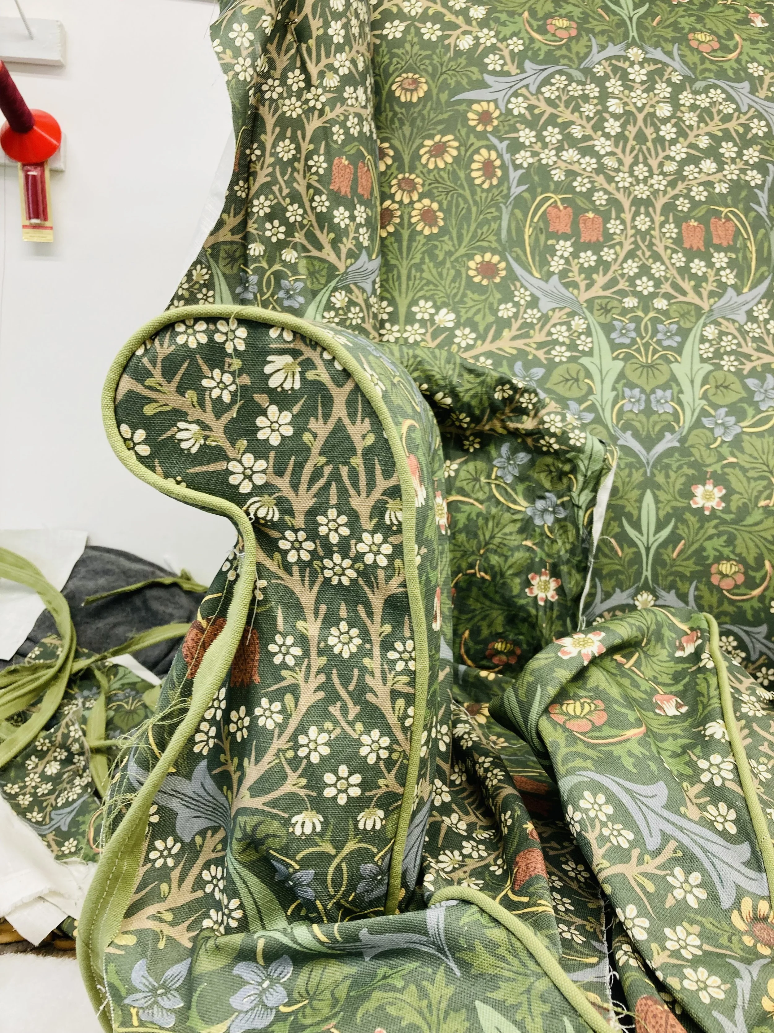 A fabric with a floral pattern featuring green, beige, and hints of red and blue colors, draped and partially covering a chair.