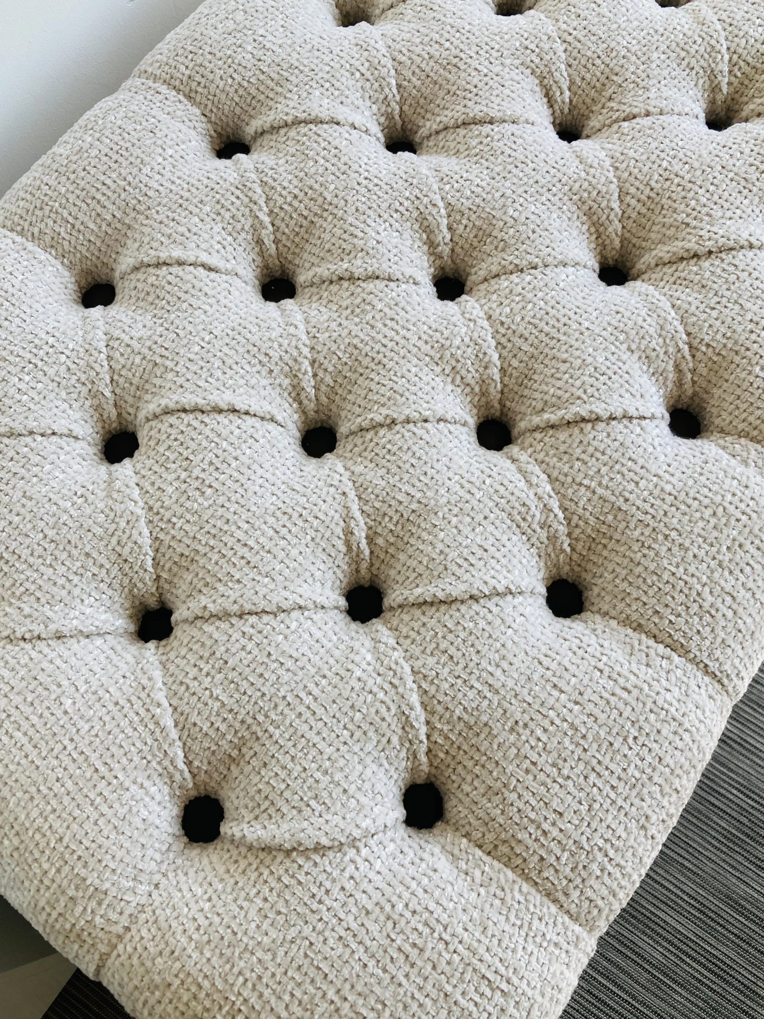 A close-up of a tufted, cream-colored textured fabric surface with black circular elements at each intersection, possibly part of a piece of furniture or decorative cushion.