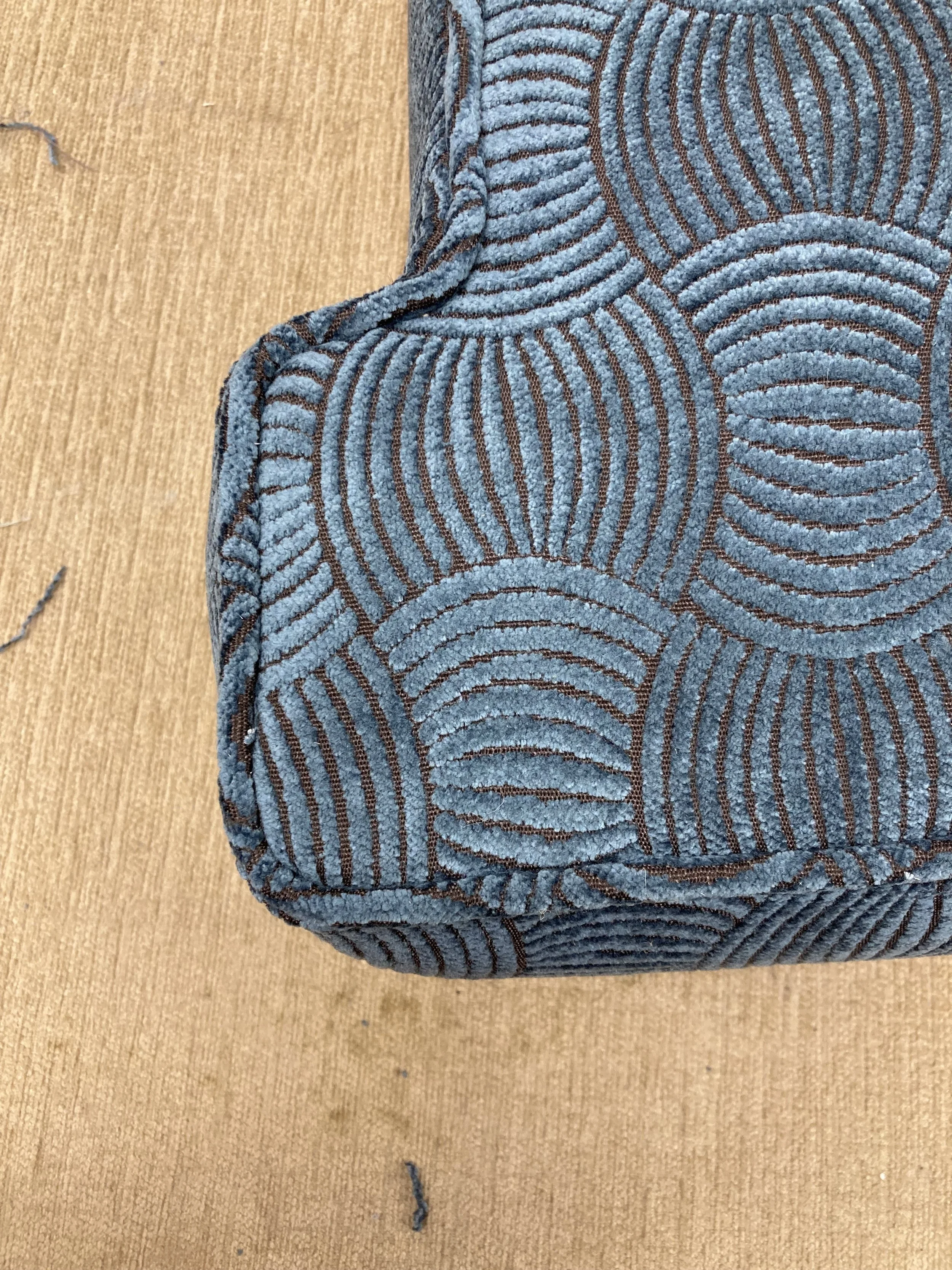 Close-up of a blue and brown patterned fabric item, possibly a knitted or woven piece, resting on a wooden surface.