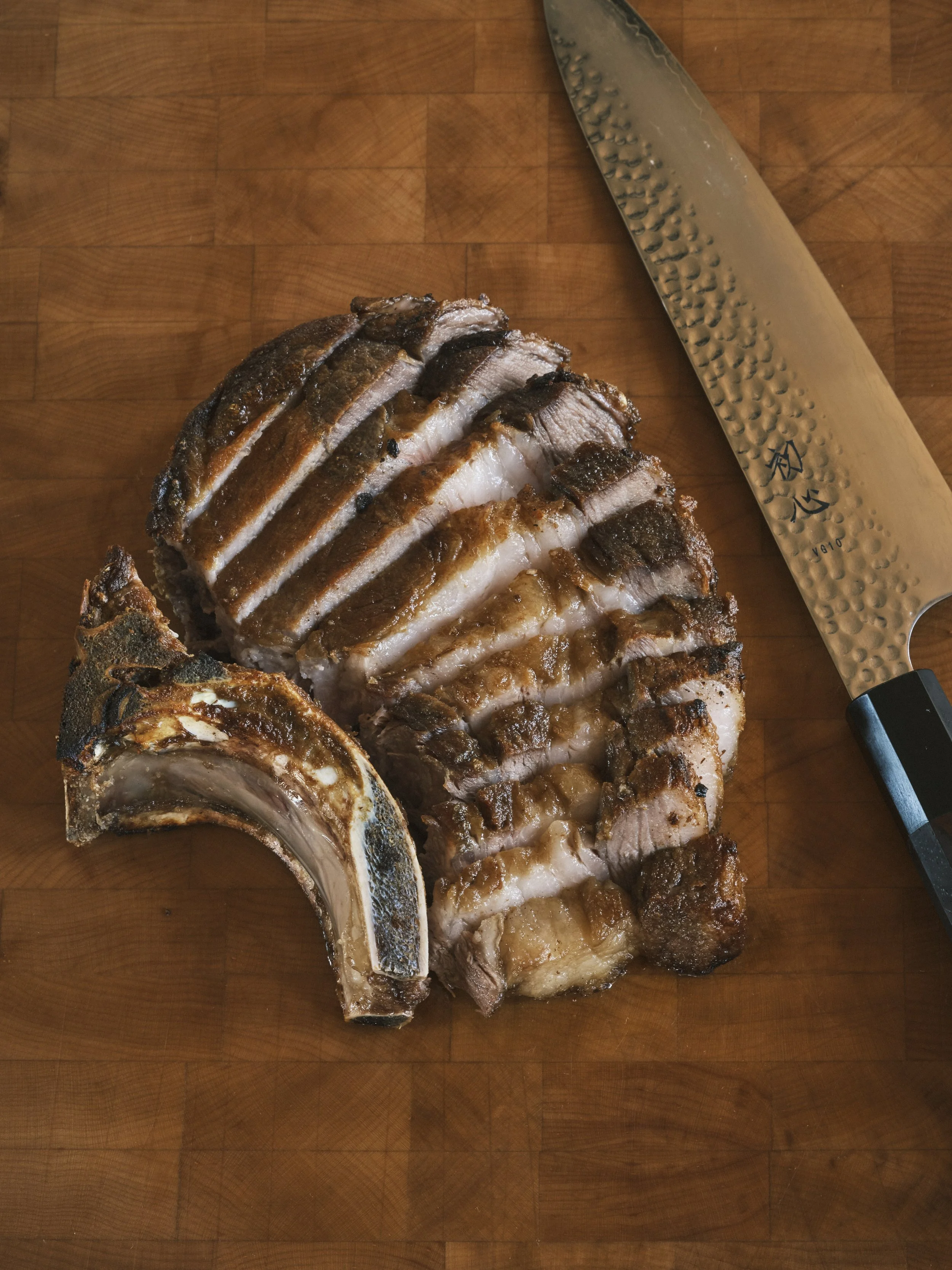 Sliced cooked brisket on a wooden cutting board with a large kitchen knife.
