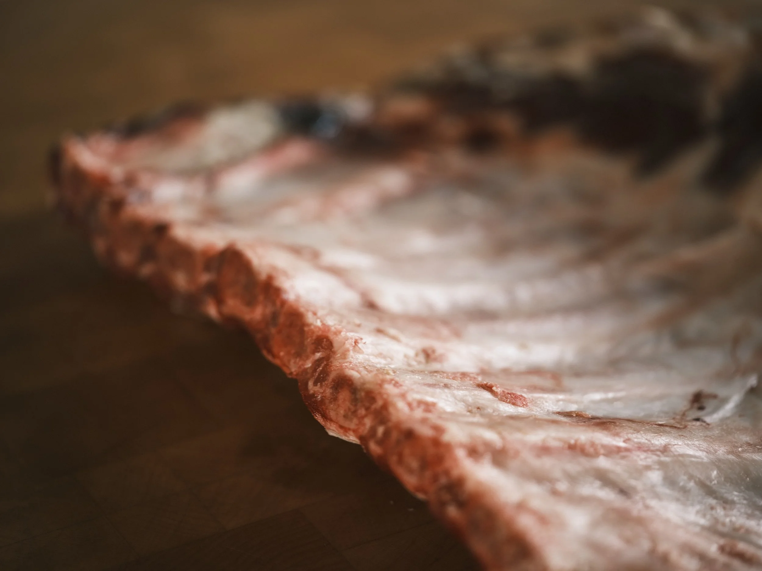 Close-up of a raw oyster shell with a rough, ridged exterior, resting on a wooden surface.