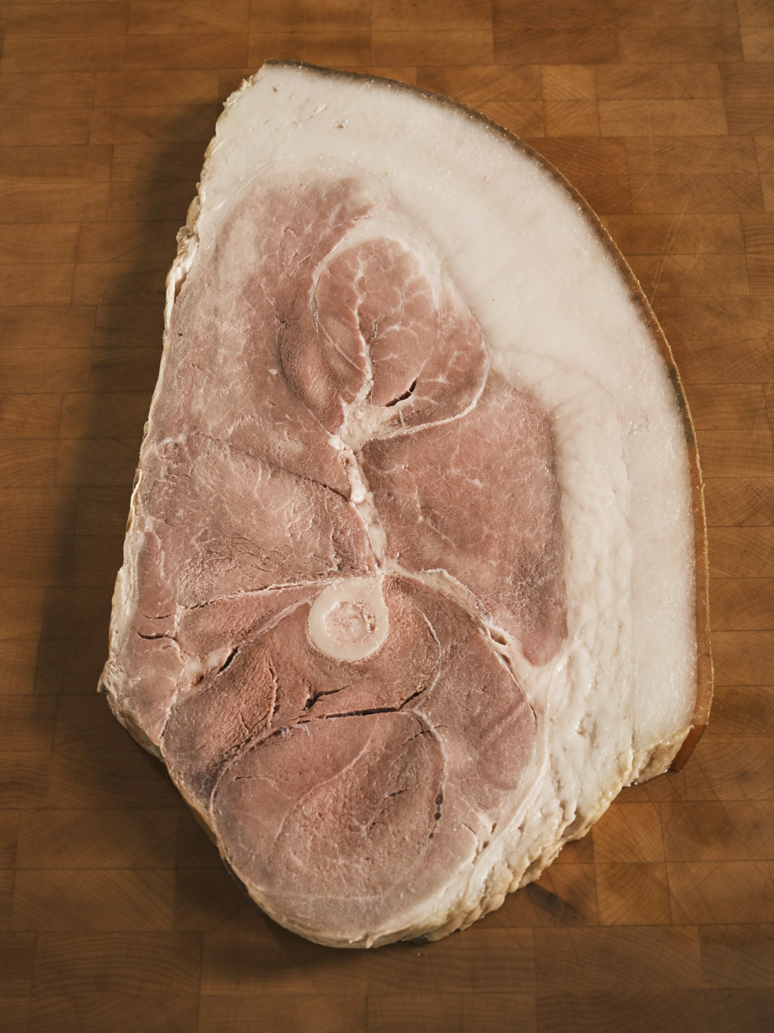 A large cut of meat with marbling and bone, placed on a wooden cutting board.