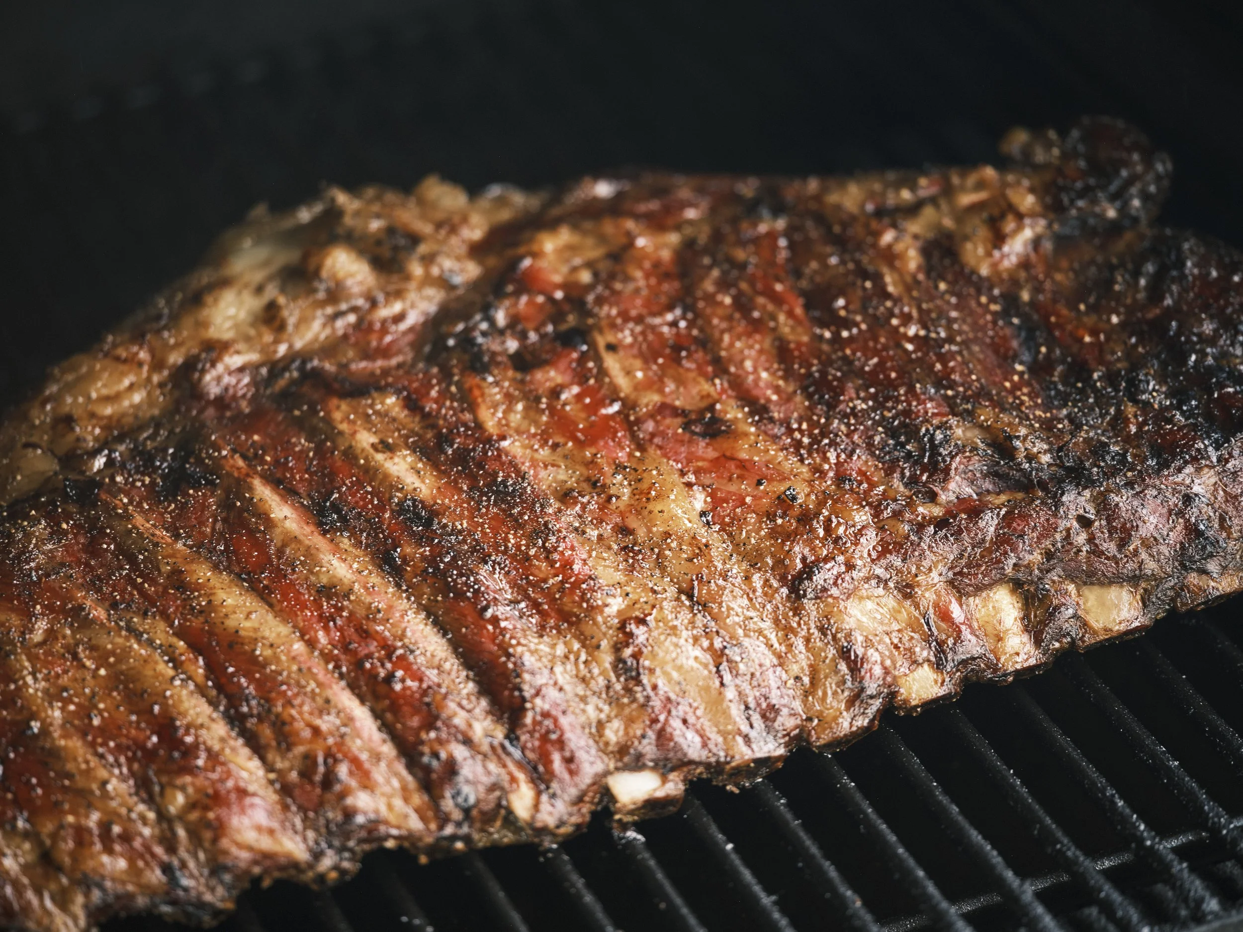 A close-up of a grilled steak with grill marks, seasoned with salt, cooking on a grill.