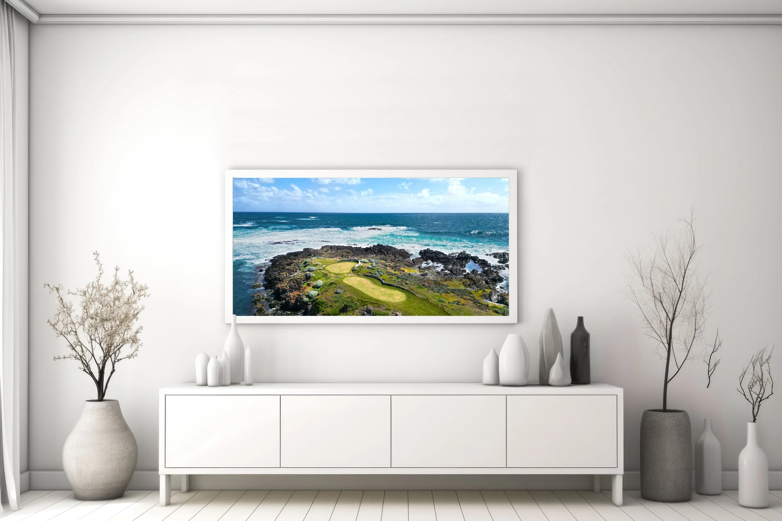Modern living room with white furniture, black and white vases, and minimalist decor, featuring a large framed landscape photo of the ocean and rocky coastline on the wall.