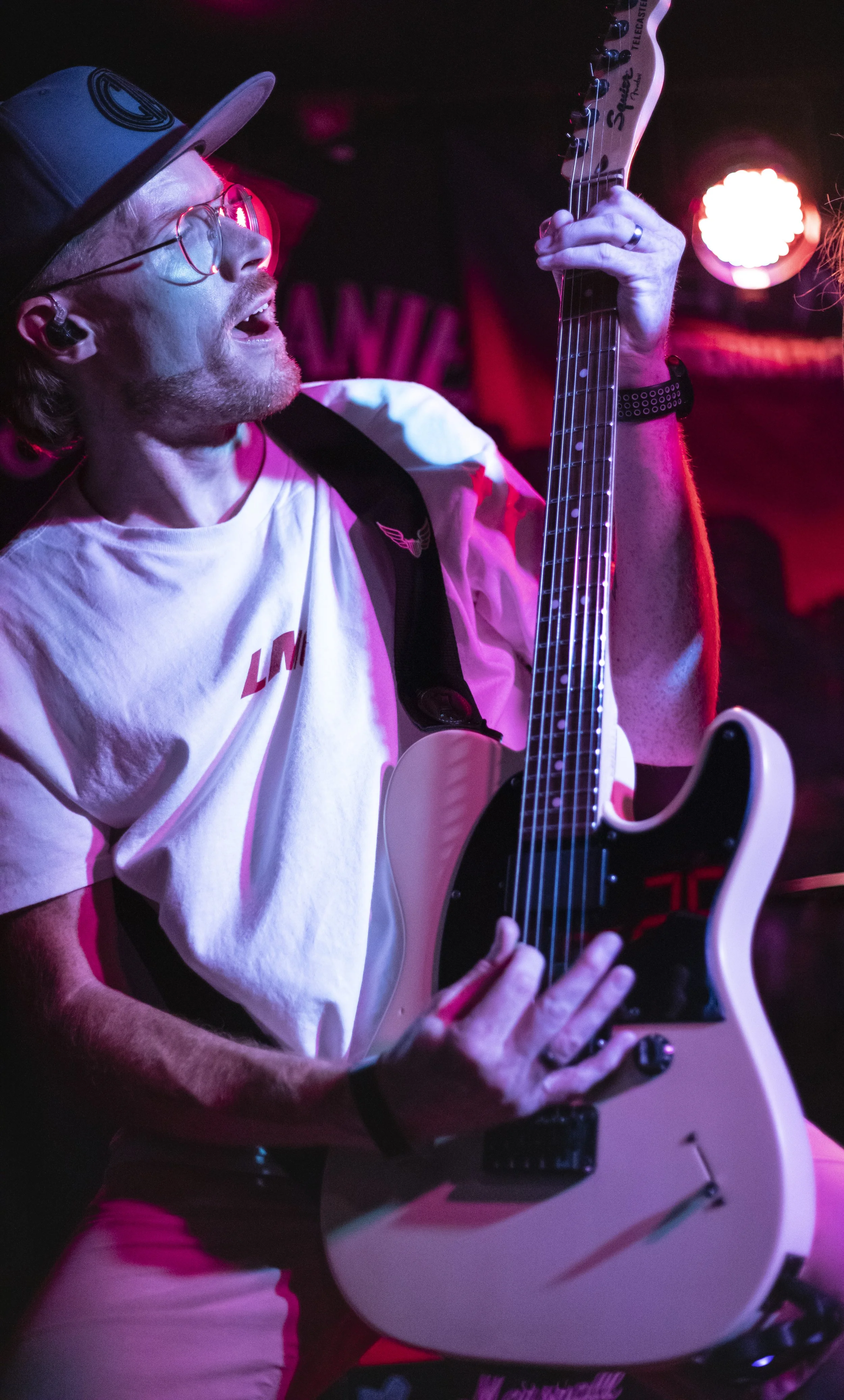 A man playing an electric guitar on stage, with colorful stage lighting highlighting him.