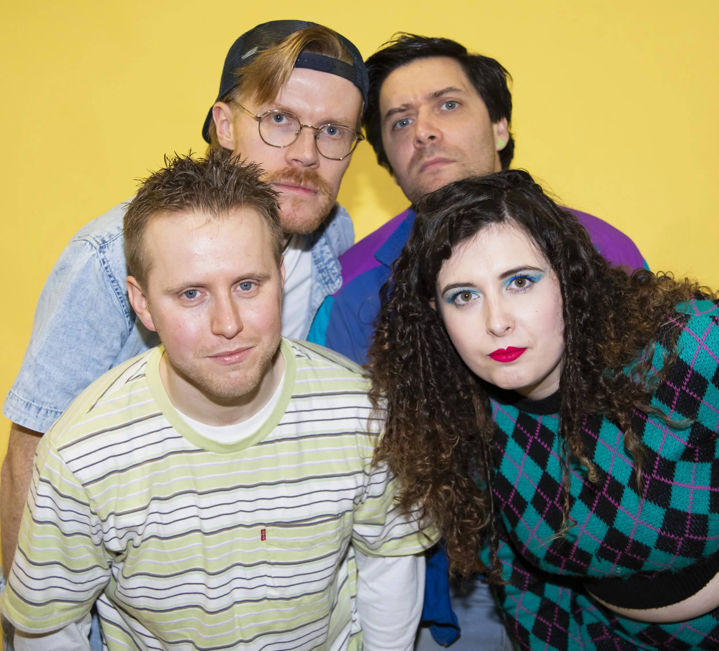 Group of five people posing against a yellow background.
