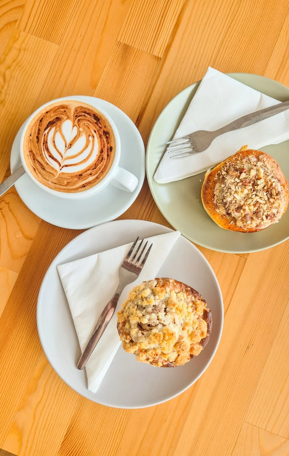 A cup of hot chocolate with foam art, two muffins on plates with forks, on a wooden table. Discover Alvor - best spots to eat, drink, and experience on your holiday.
