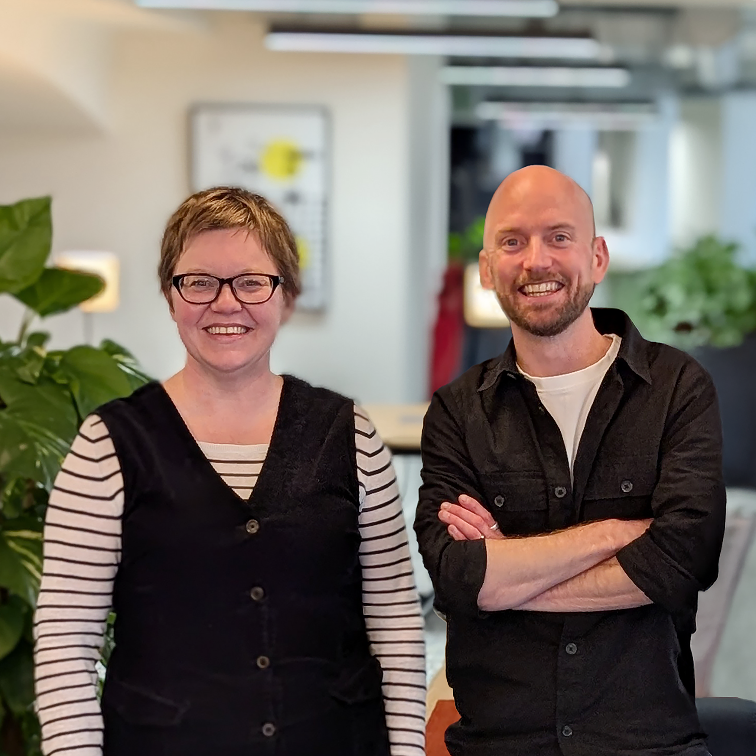 Stone Lane Architects Ltd — A woman with short brown hair, glasses, and a striped shirt under a black vest, standing next to a bald man with a beard, wearing a black shirt and sm
