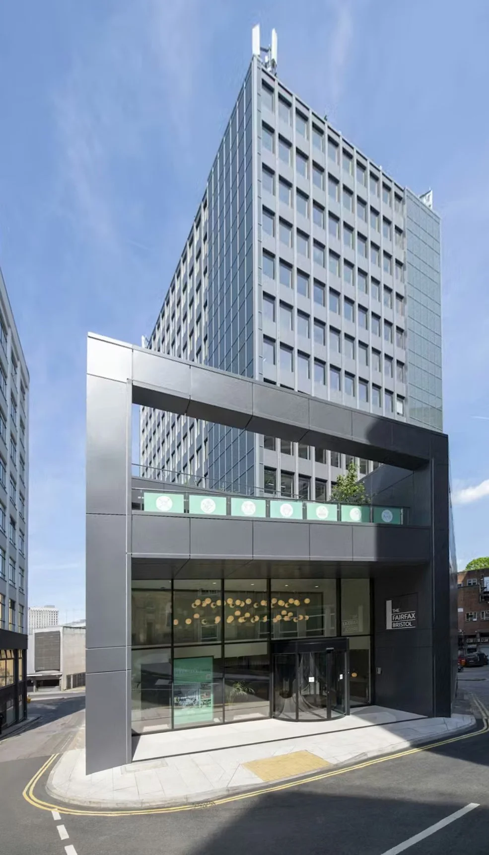 Modern high-rise office building with a black entrance archway and glass facade, located on a corner street with a clear blue sky above.