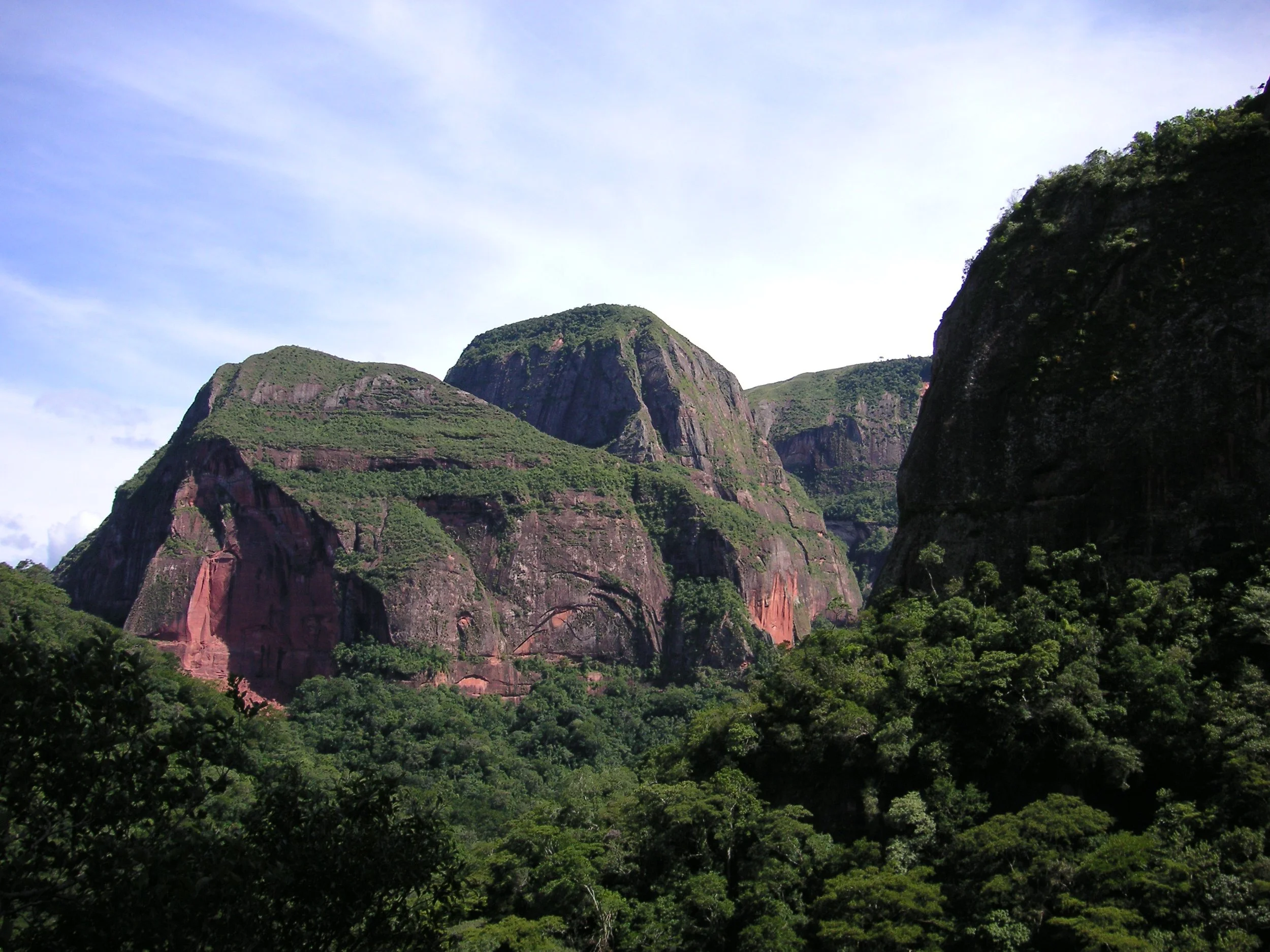 Berglandschaft mit grünen Hügeln, Felsen und bewaldeten Flächen unter blauem Himmel.