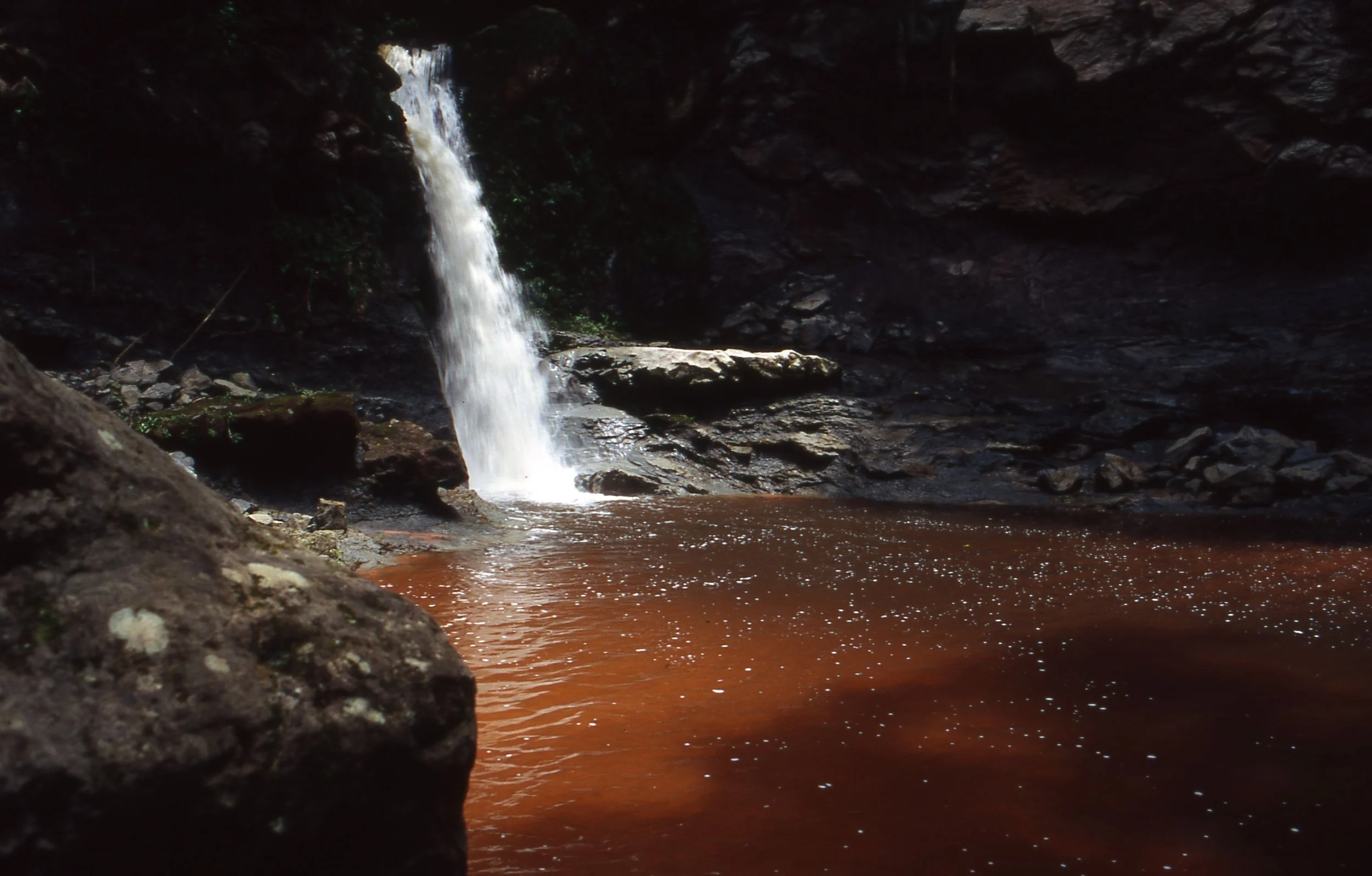 Kleiner Wasserfall fließt in einen braunen Fluss in einer dunklen Höhle.